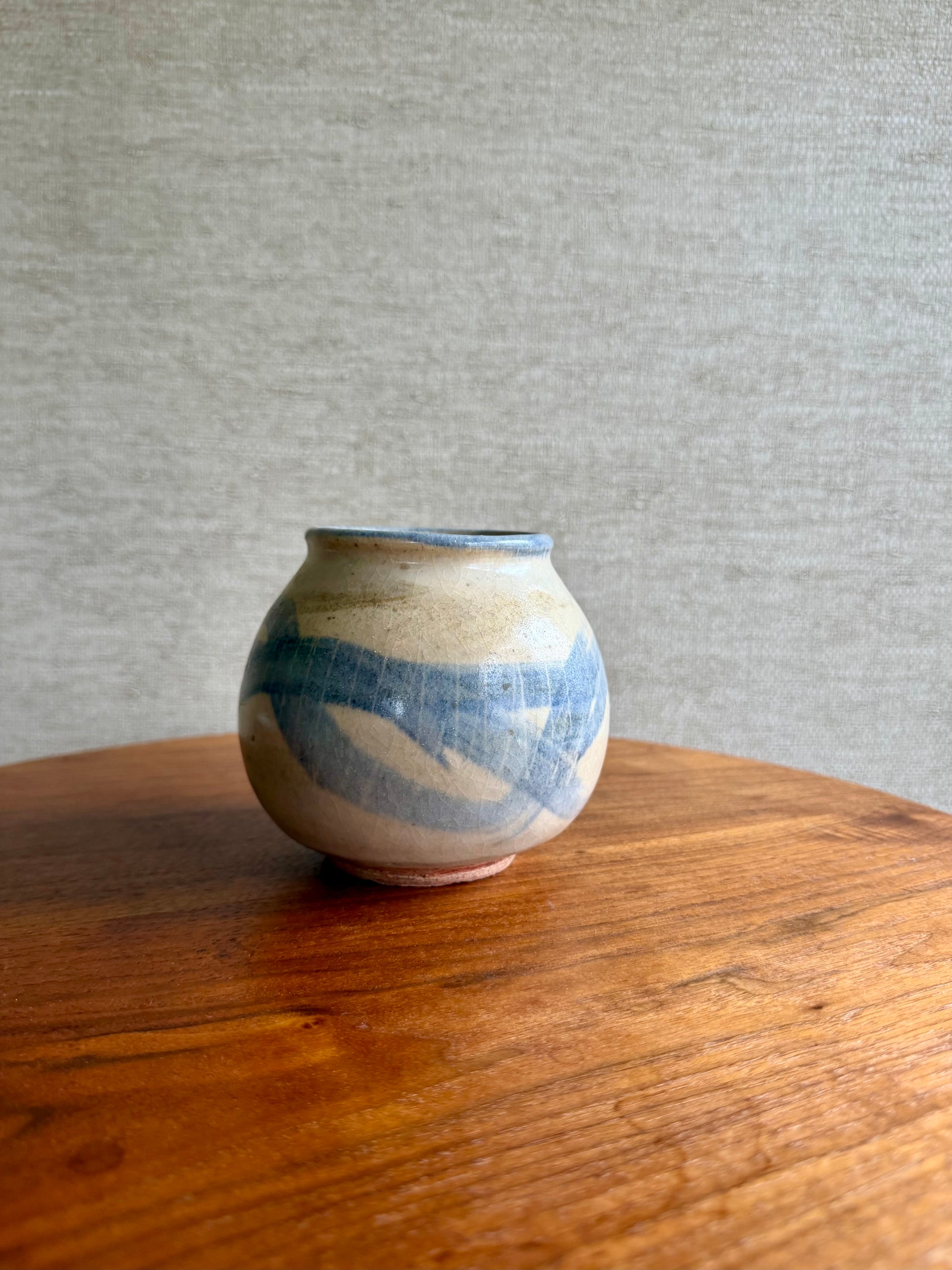 Small ceramic vase with blue and beige patterns on a wooden surface and gray background