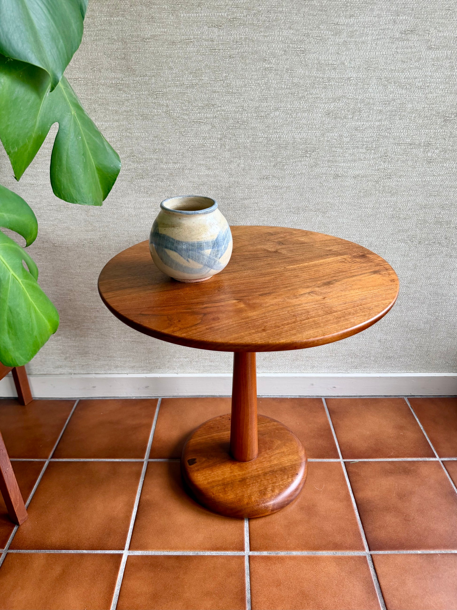 Wooden side table with a ceramic vase on a tiled floor against a textured wall.