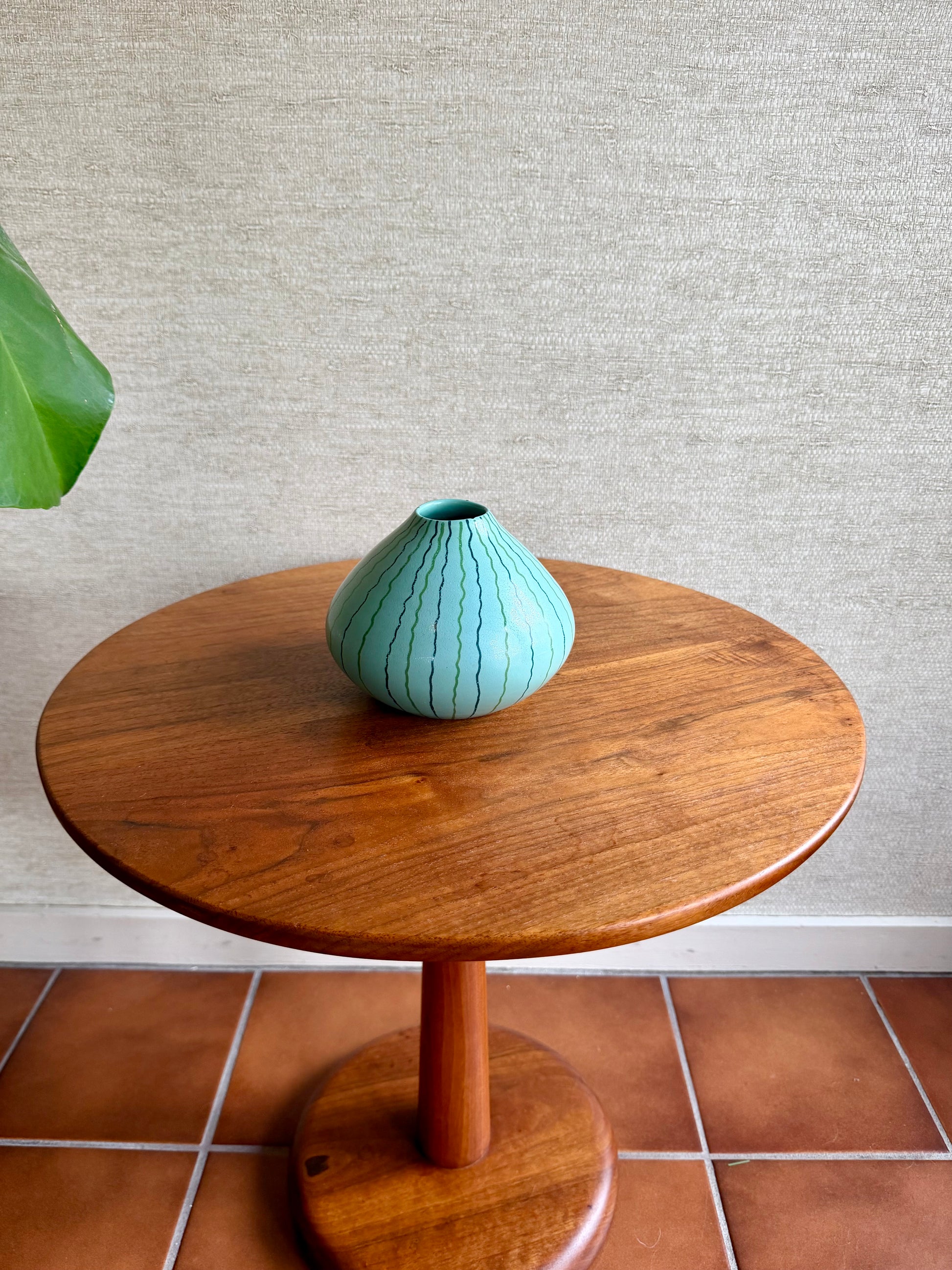 Teal vase on a wooden side table against a textured wall.