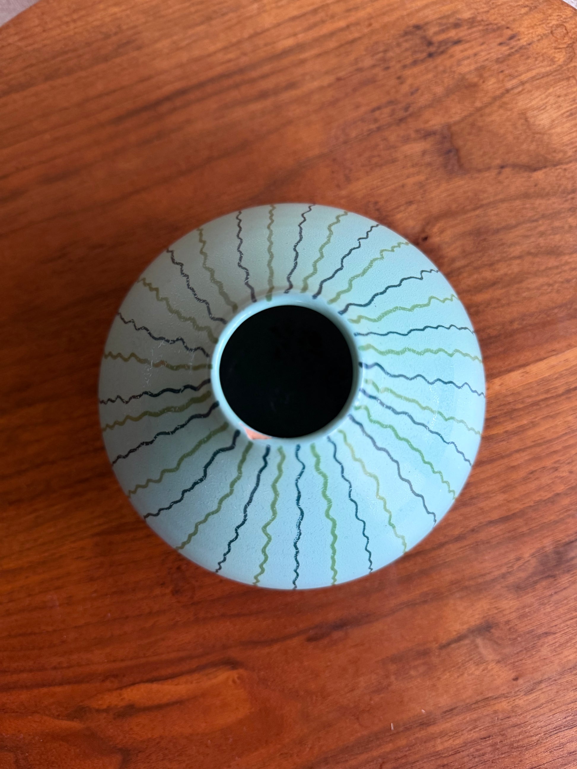 White vase with wavy black and green design on a wooden surface