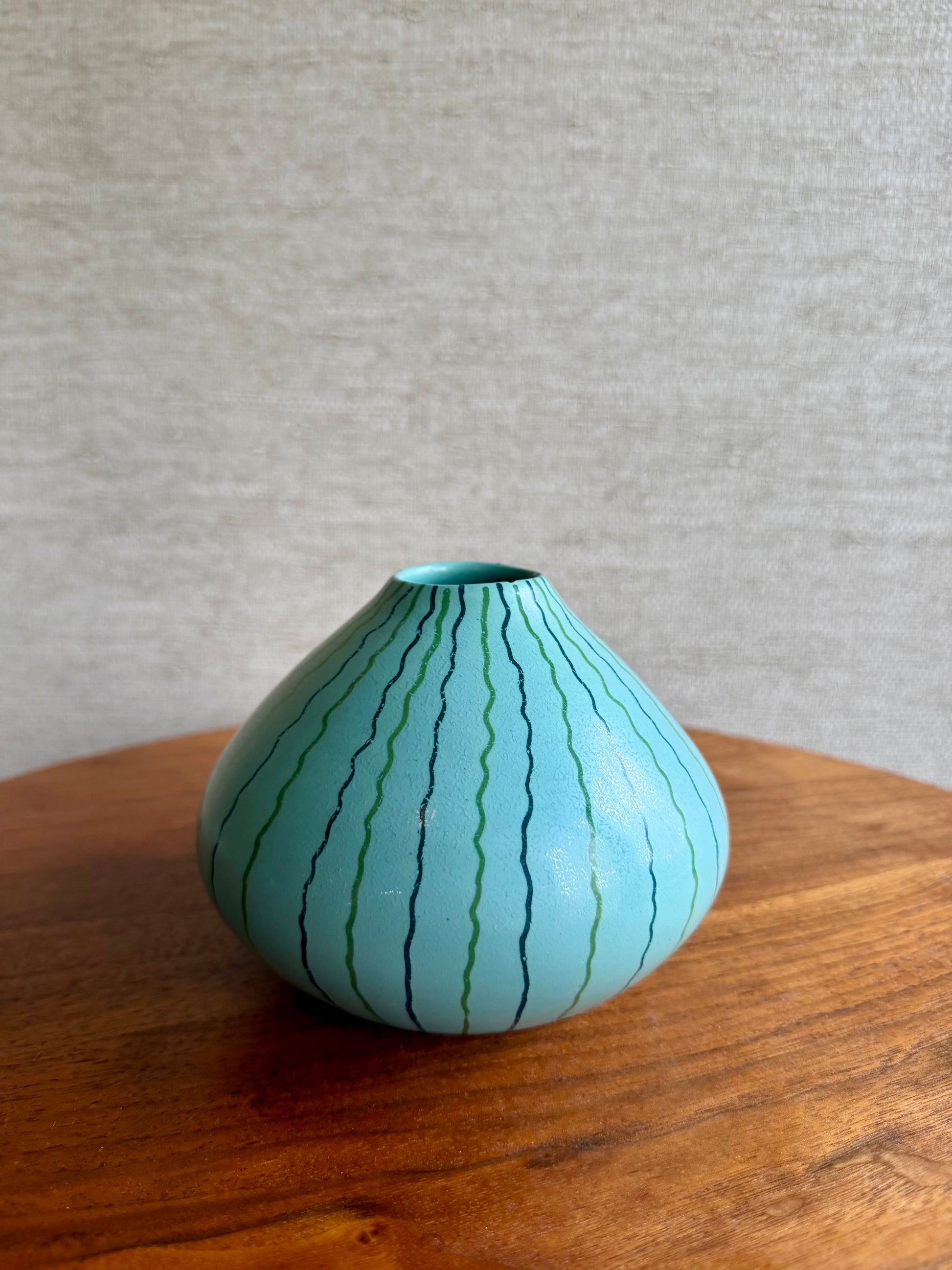 Light blue ceramic vase with green stripes on a wooden surface and gray background