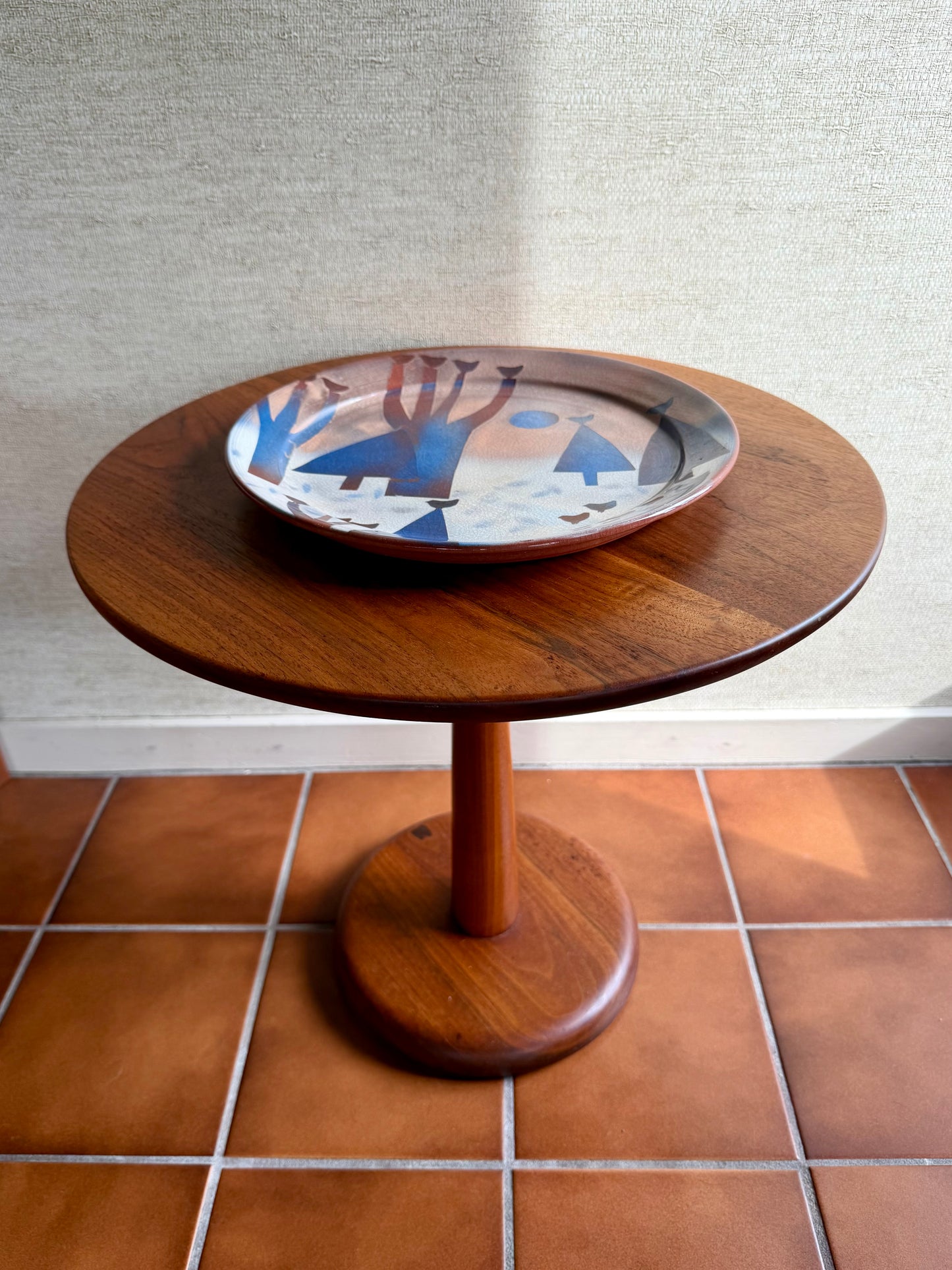 Wooden side table with a decorative plate on a tiled floor