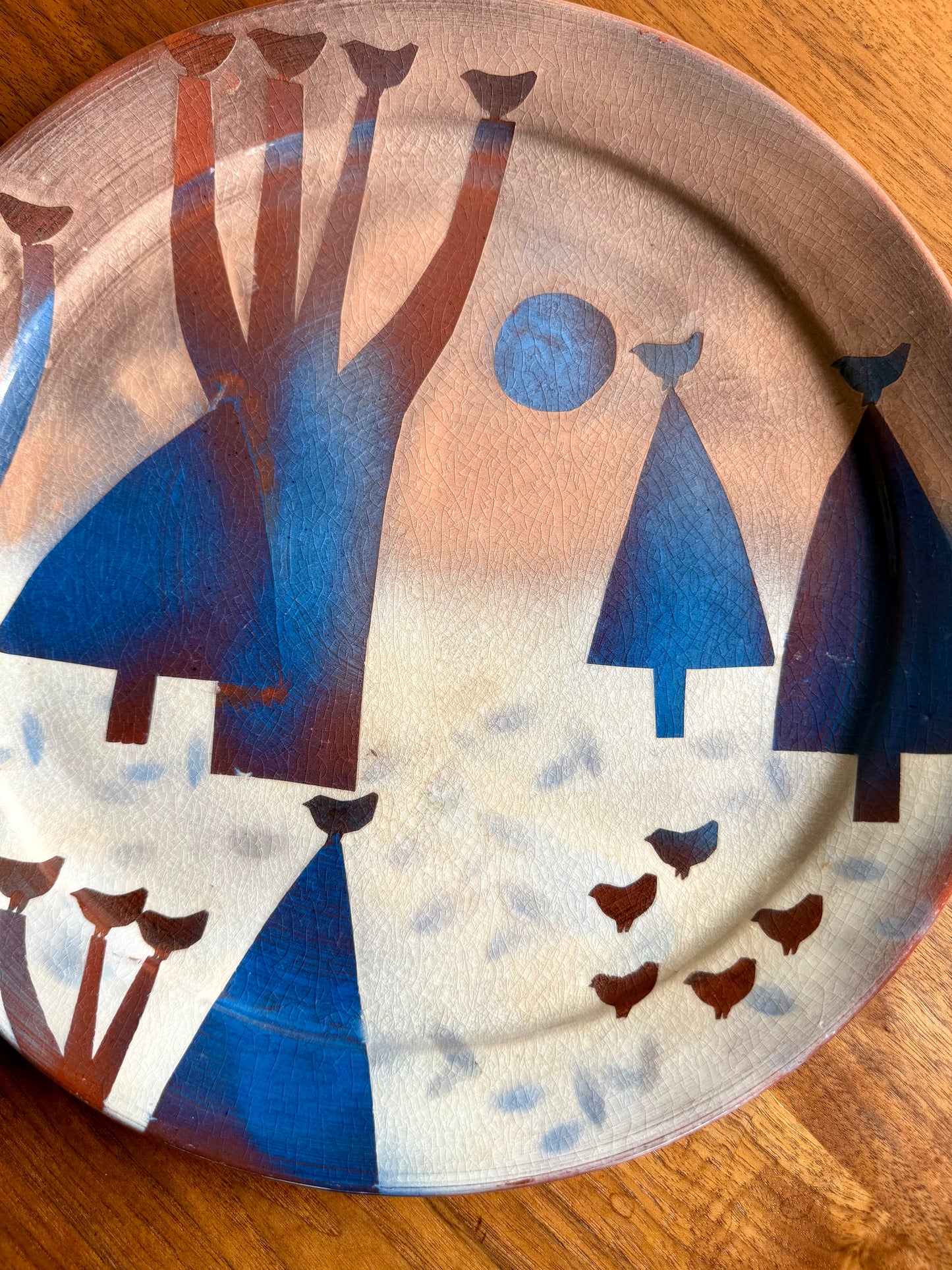 Decorative plate with abstract human figures and animals on a wooden surface
