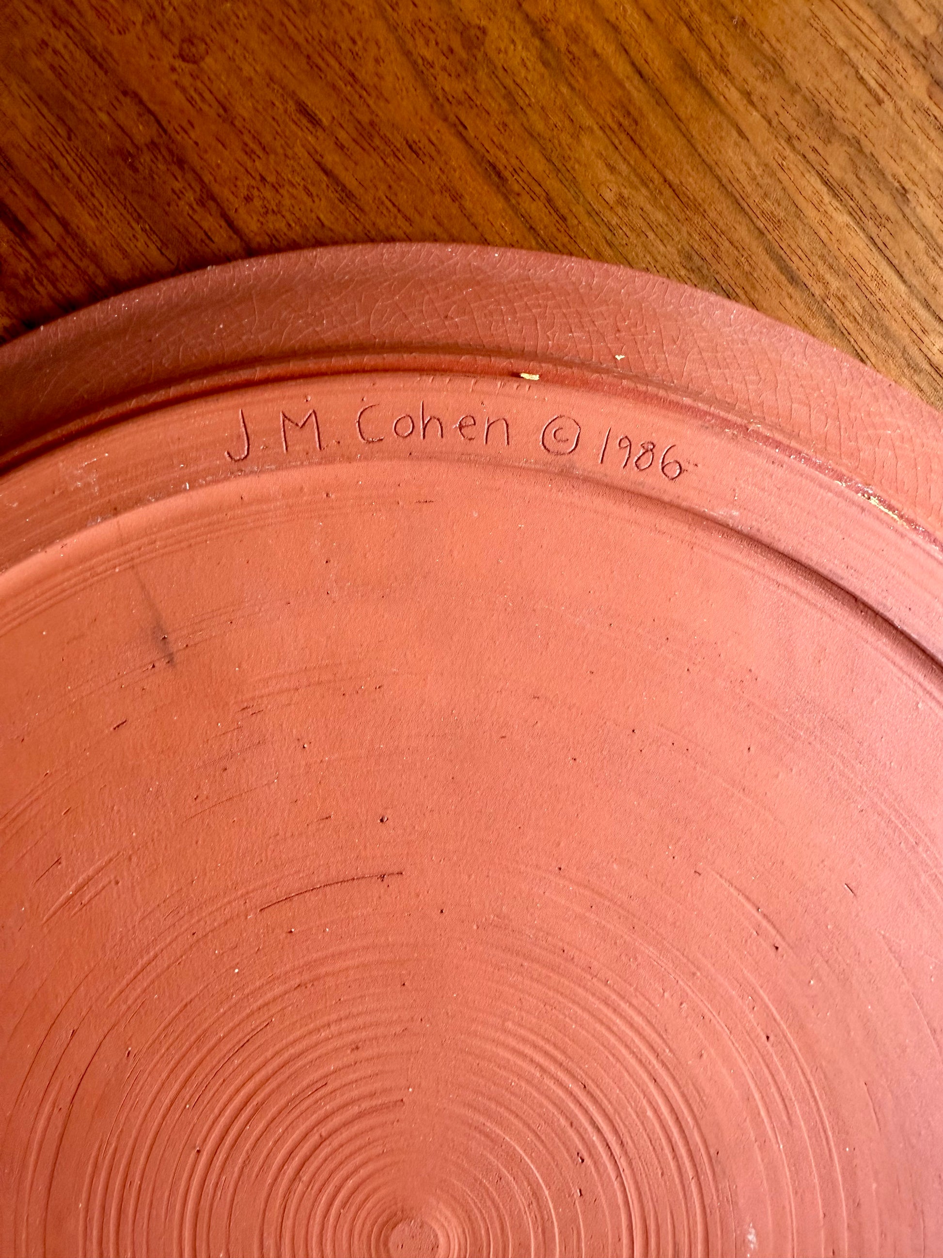 Terracotta pot with 'J. M. Cohen 1986' inscription on a wooden surface