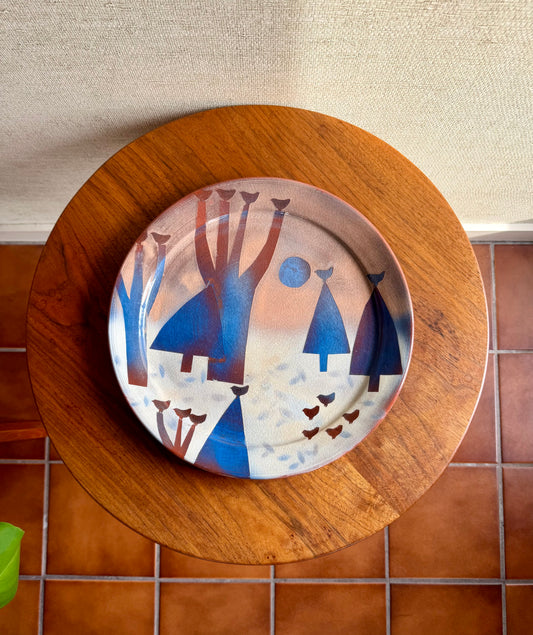 Decorative plate with abstract designs on a wooden stand against a tiled wall.