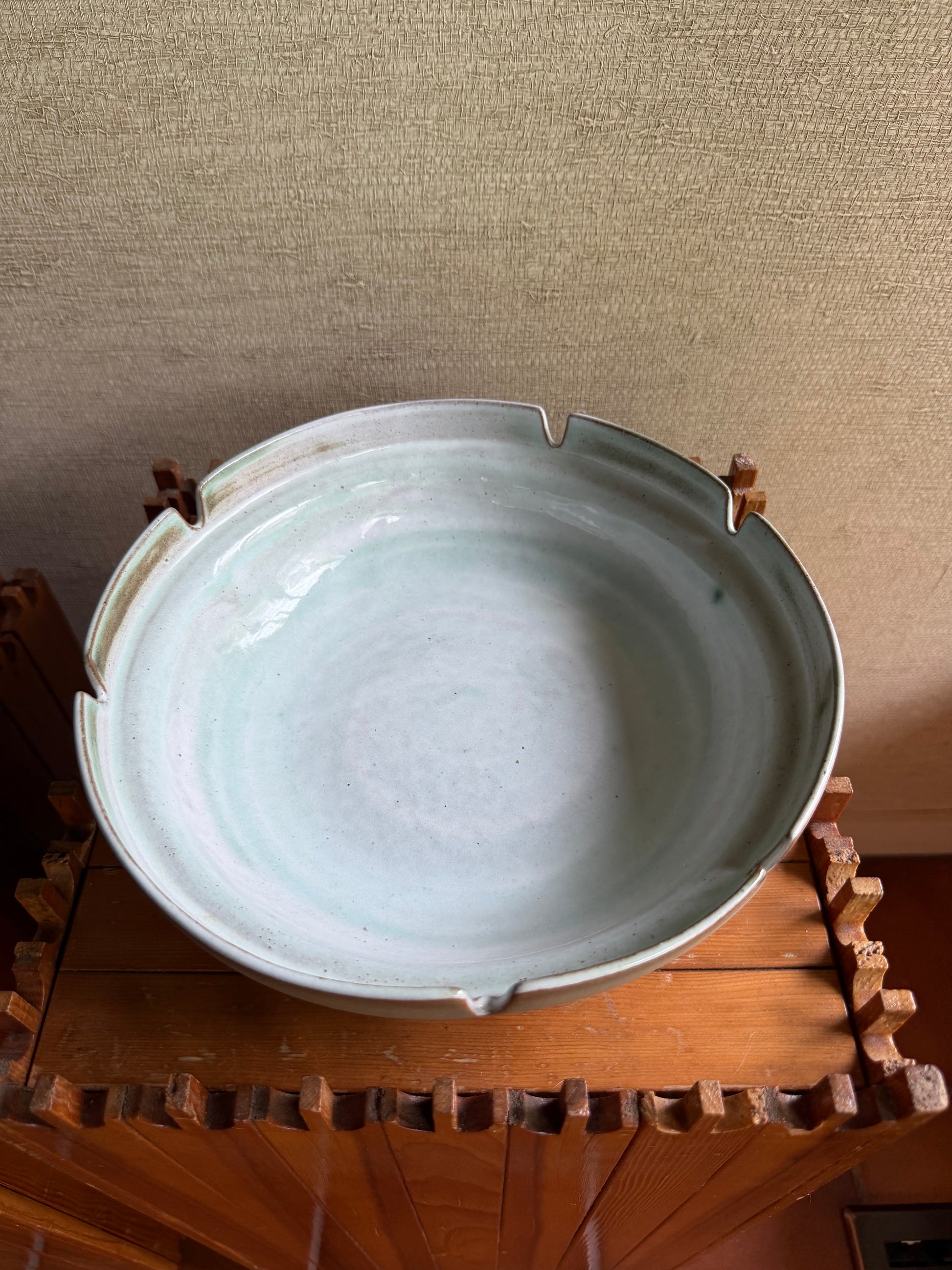 Ceramic dish with a textured surface on a wooden stand against a beige wall.