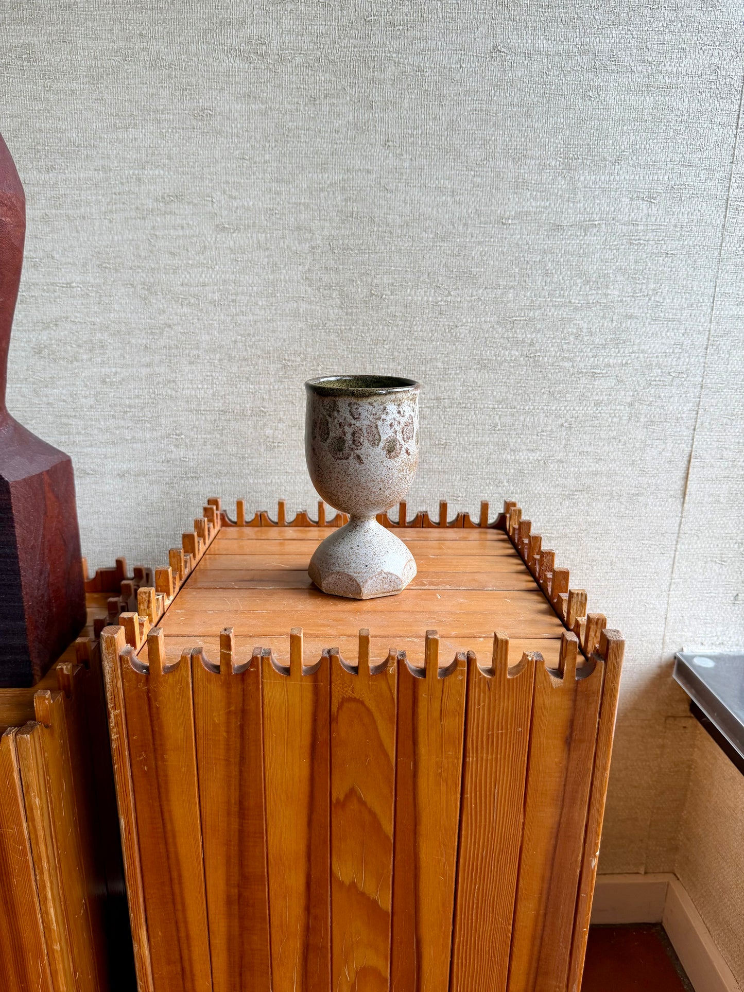 Wooden cabinet with a ceramic goblet on top against a textured wall.