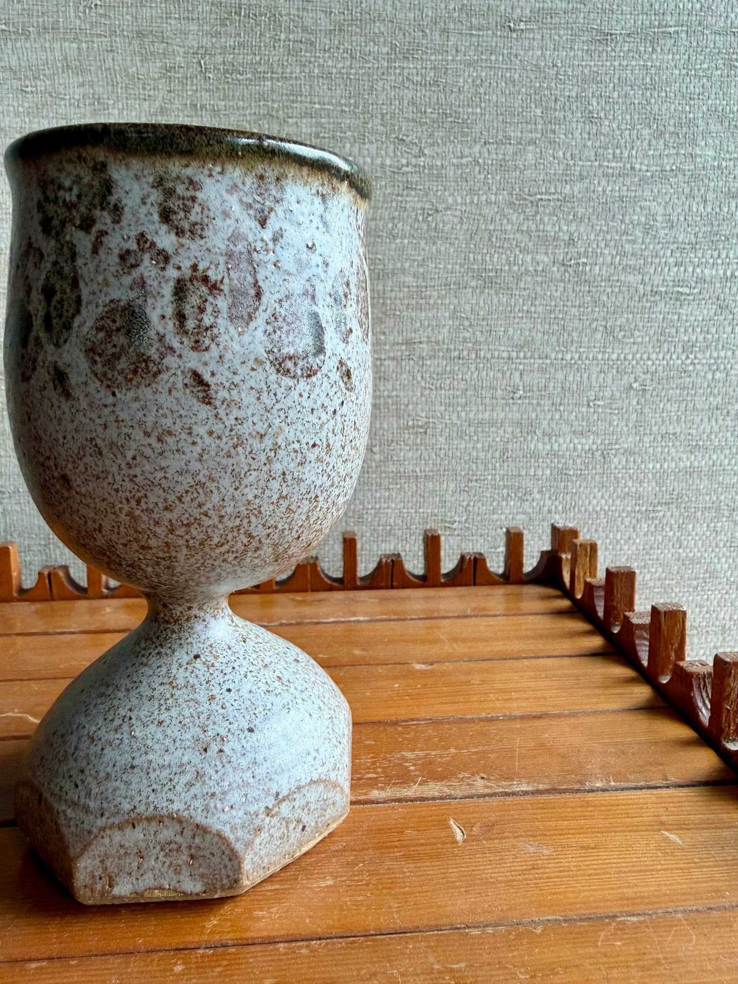 Speckled ceramic vase on a wooden surface with a textured wall background