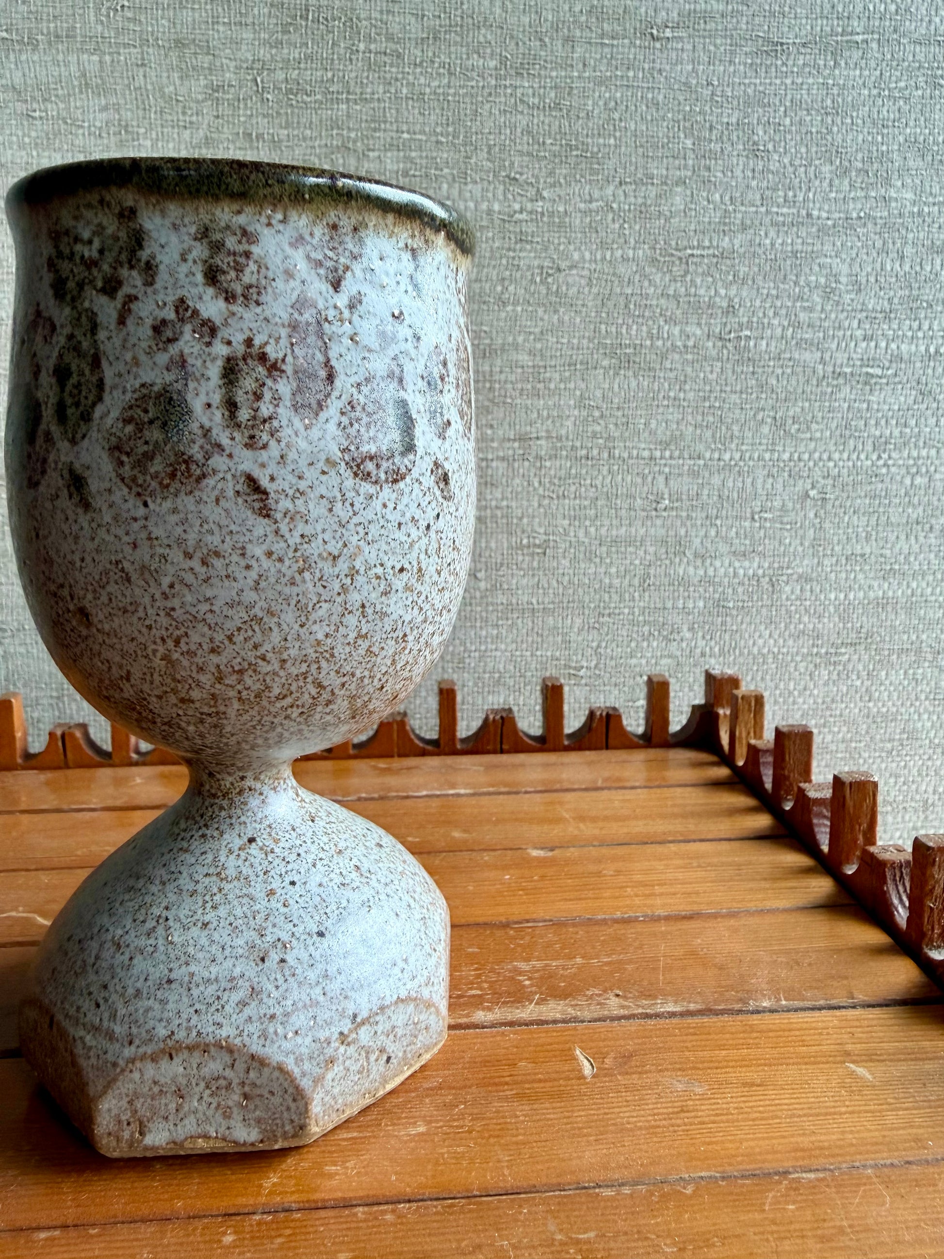 Speckled ceramic vase on a wooden surface with a textured wall background