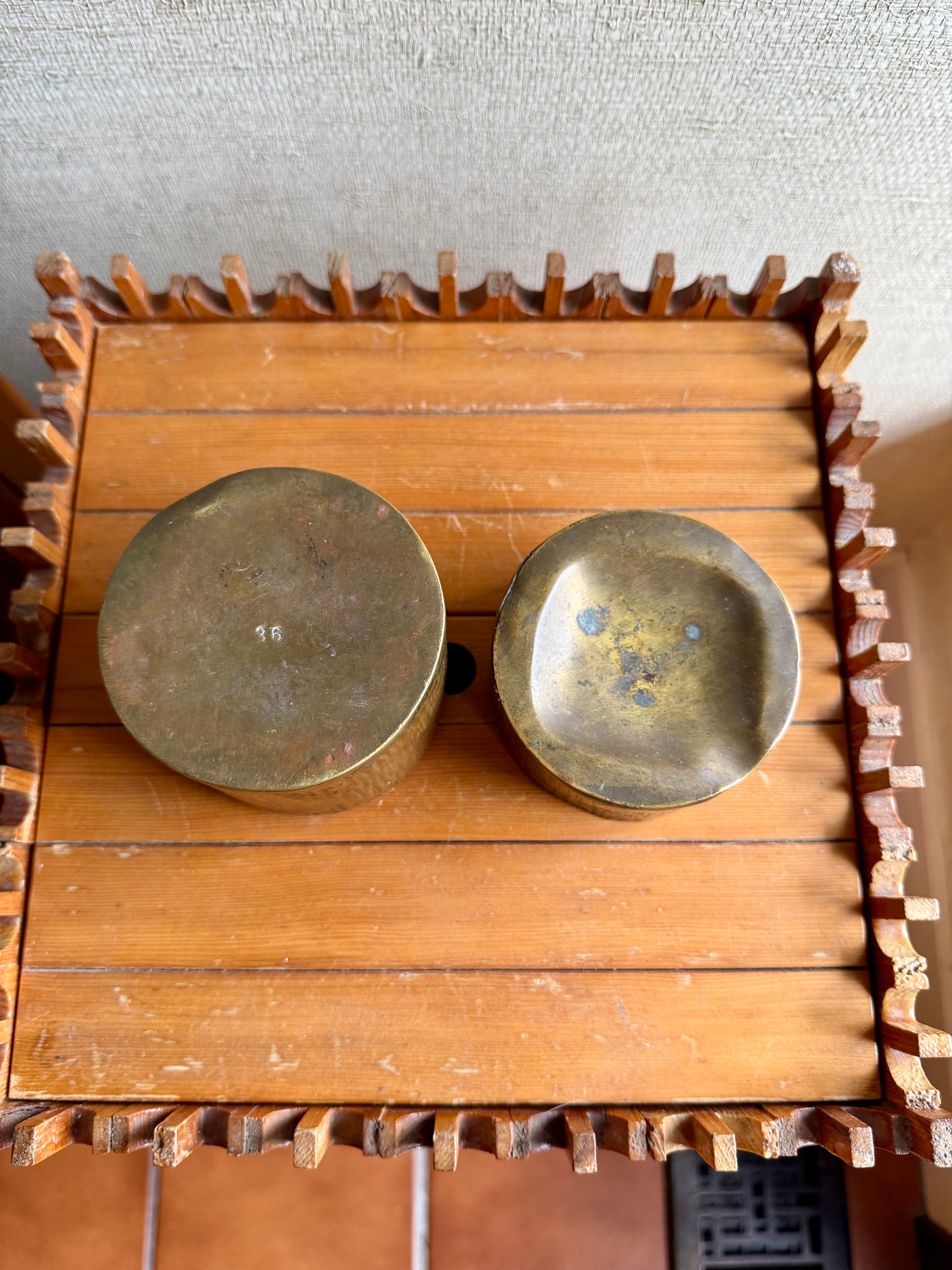 Two brass bowls on a wooden stand with a textured wall background
