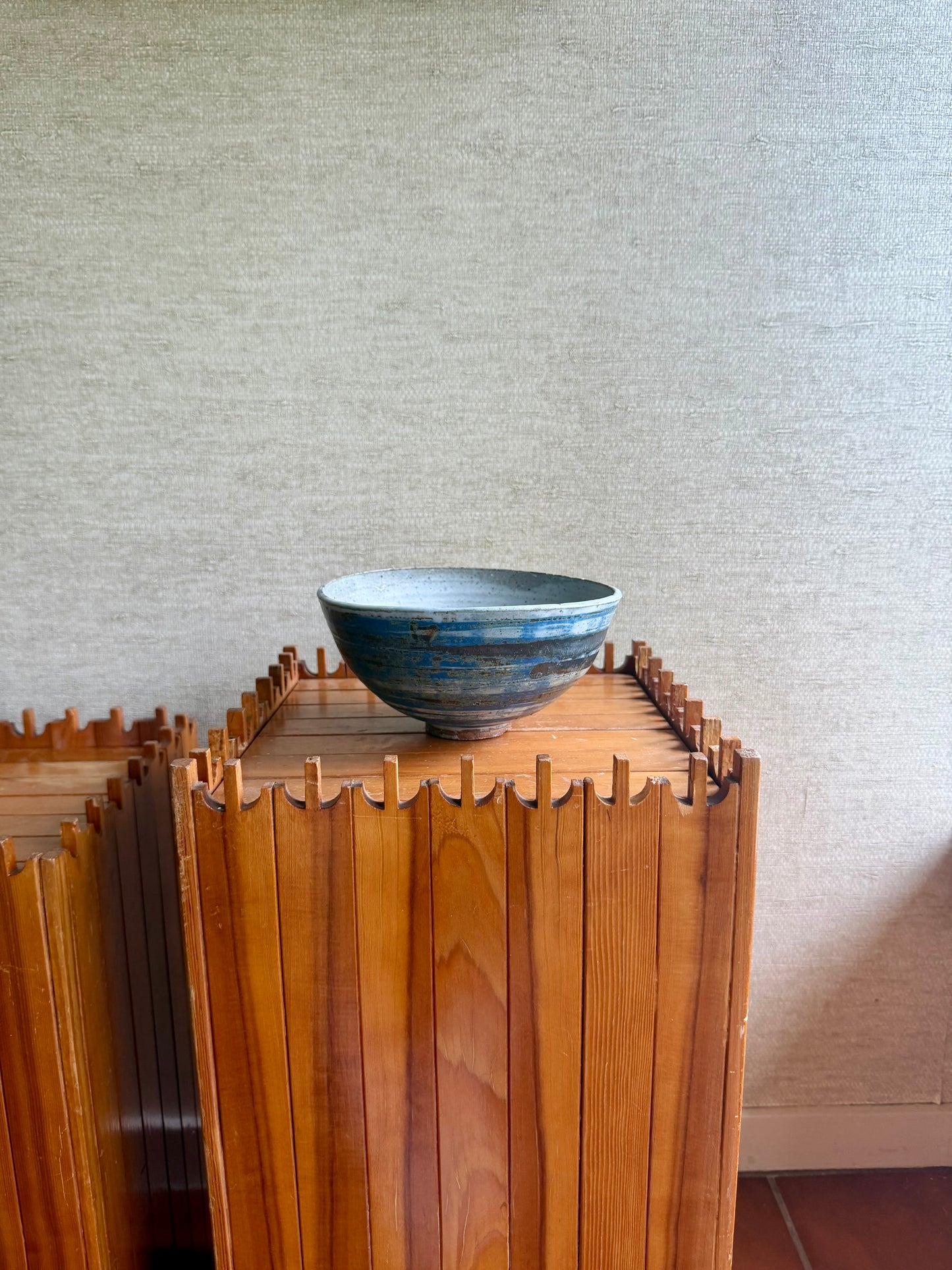 Wooden cabinet with a blue ceramic bowl on top against a textured wall.