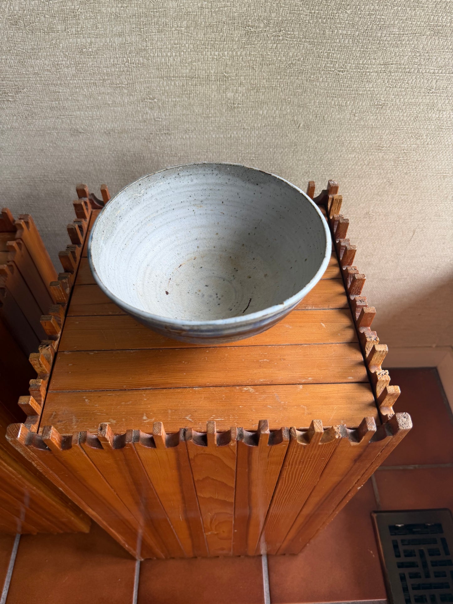 Wooden gear-like structure with a metal cylindrical component against a textured wall.