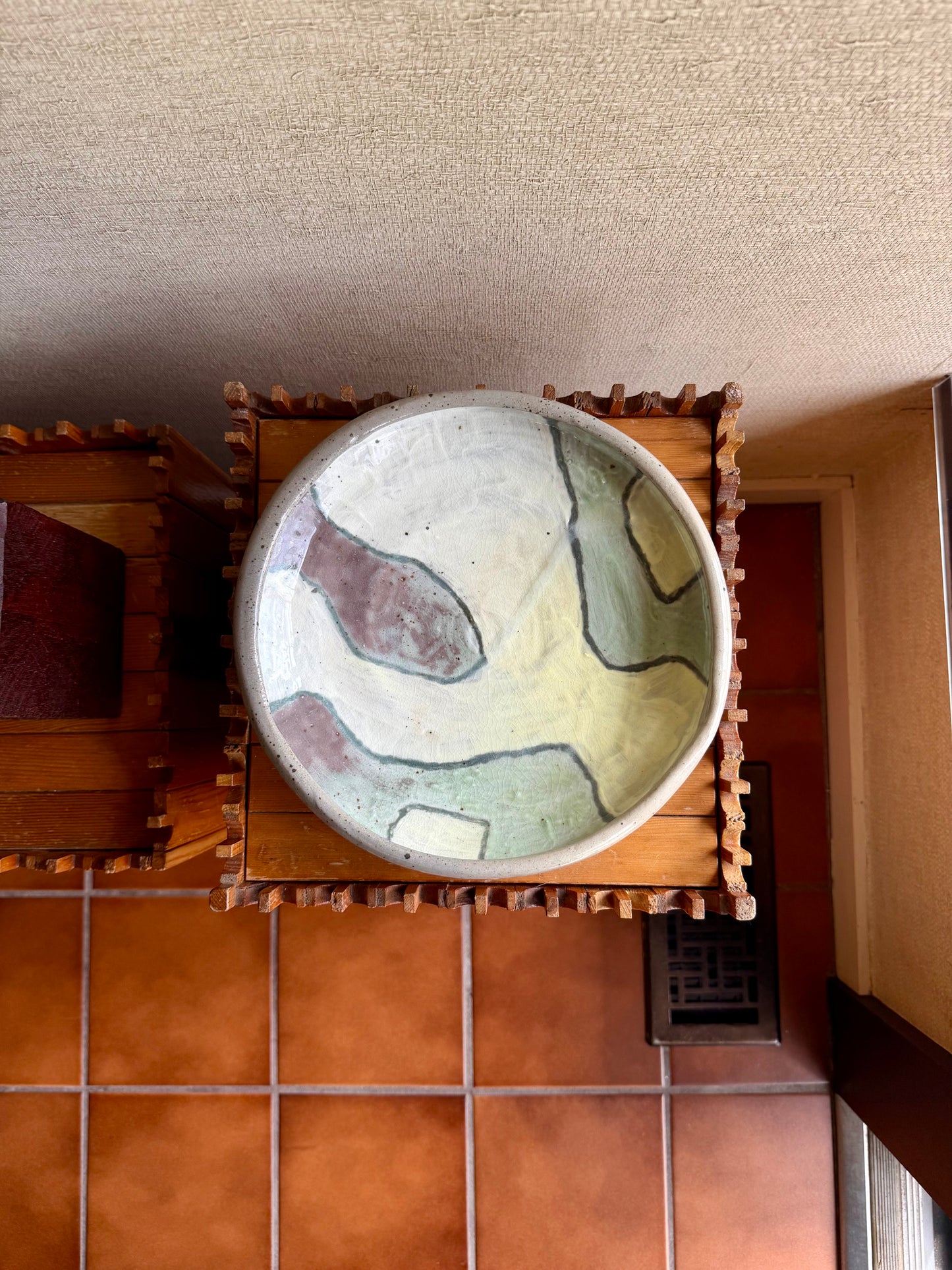 Ceramic bowl with abstract design on a wooden stand against a textured wall.