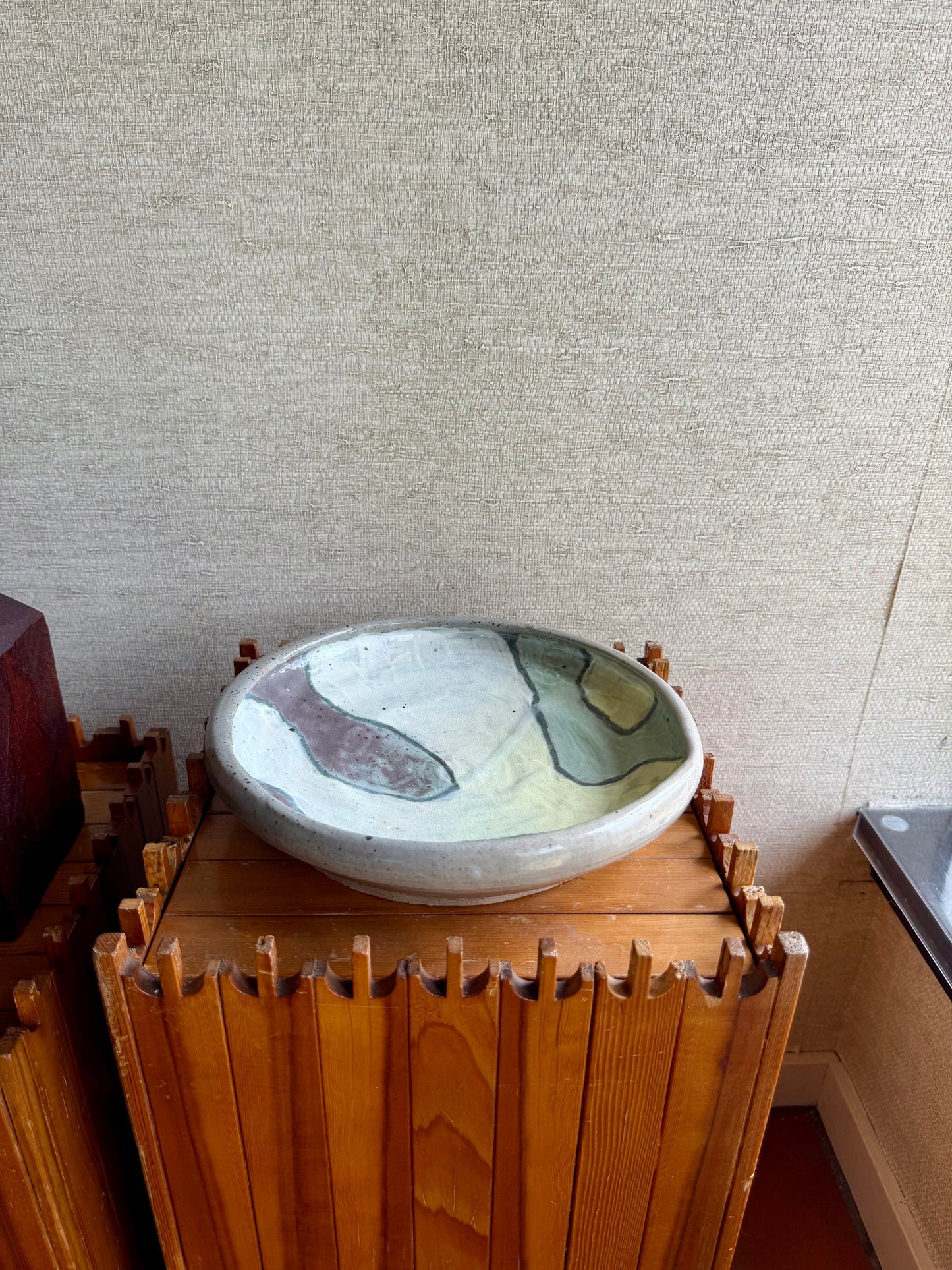 Decorative bowl on a wooden stand against a textured wall.