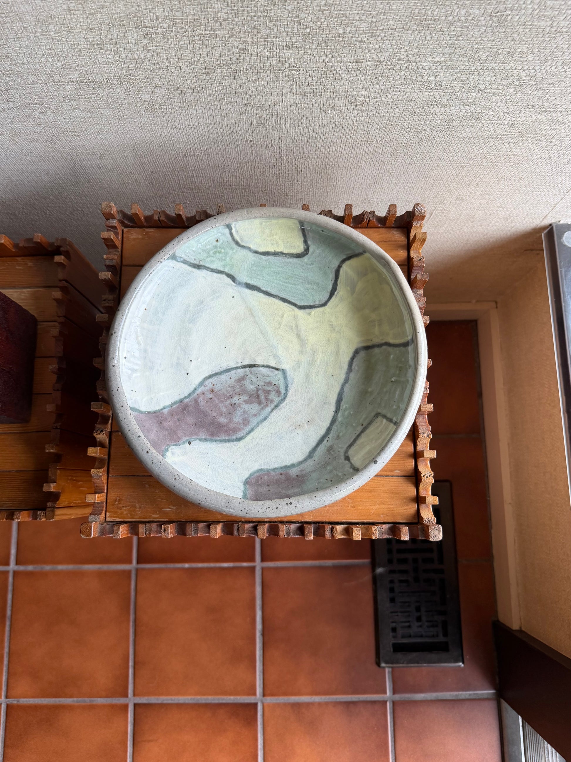 Ceramic bowl with abstract design on a wooden stand against a textured wall.