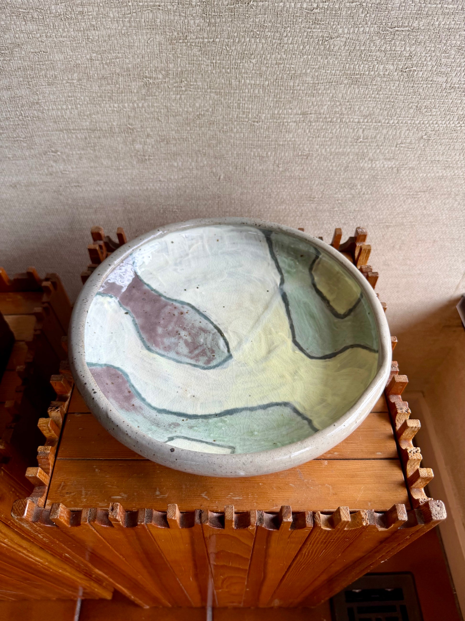 Ceramic bowl with marbled design on a wooden stand against a textured wall.