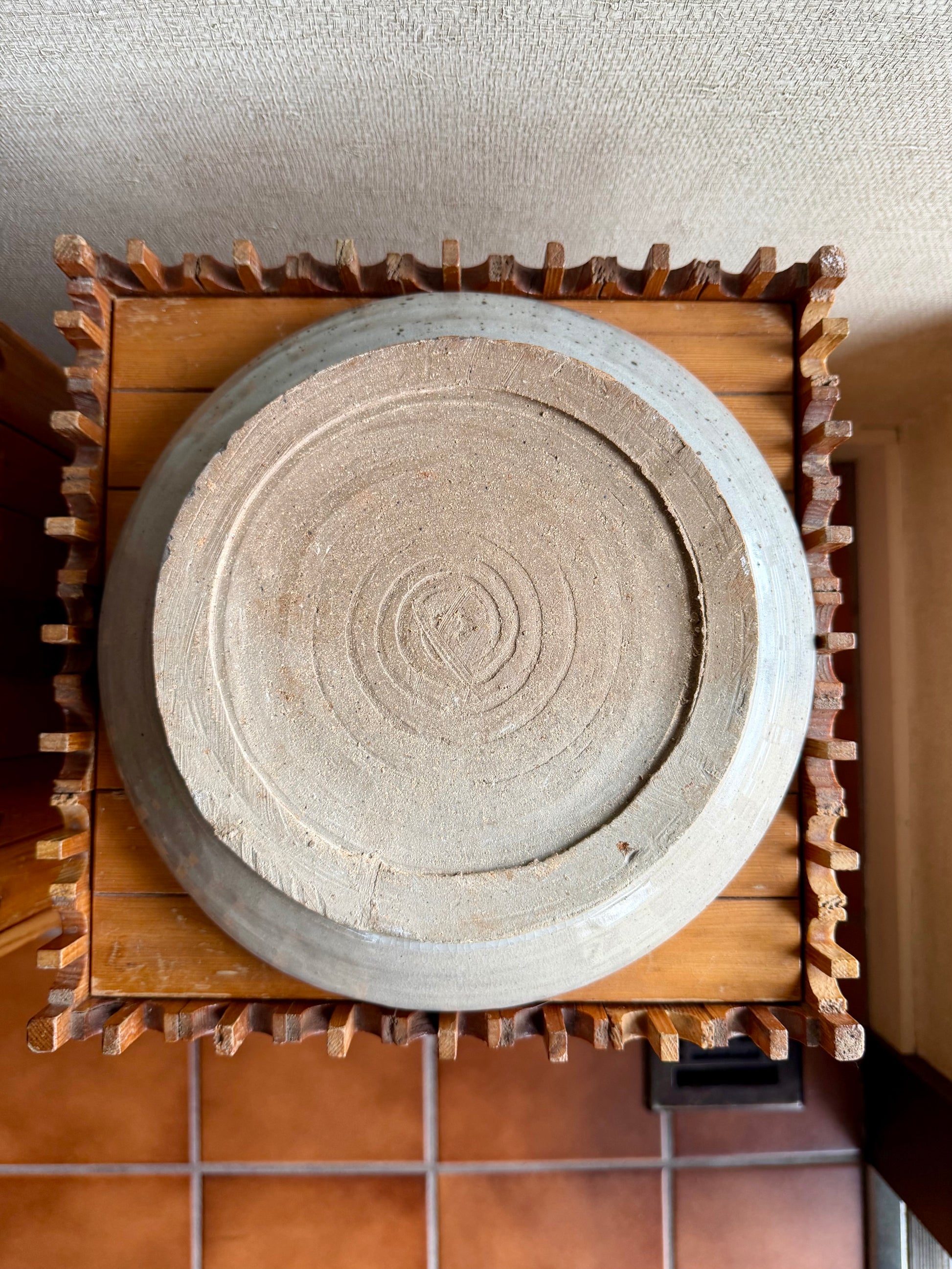 Ceramic plate with concentric circle design on a wooden stand against a textured wall.