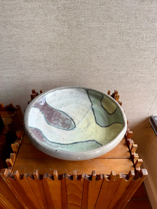 Ceramic bowl with marbled design on a wooden stand against a textured wall.