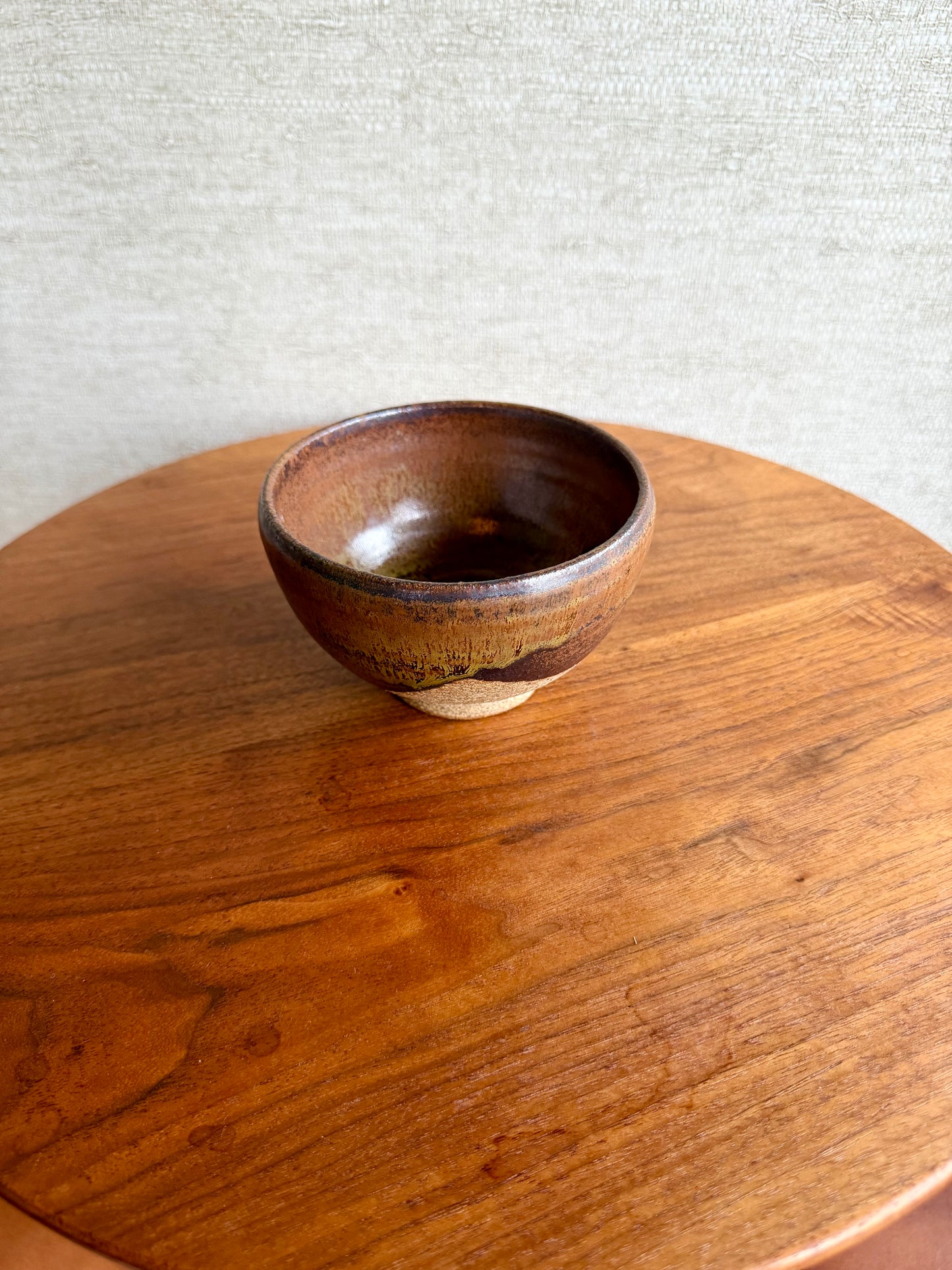 Brown ceramic bowl on a wooden surface with a light gray textured background