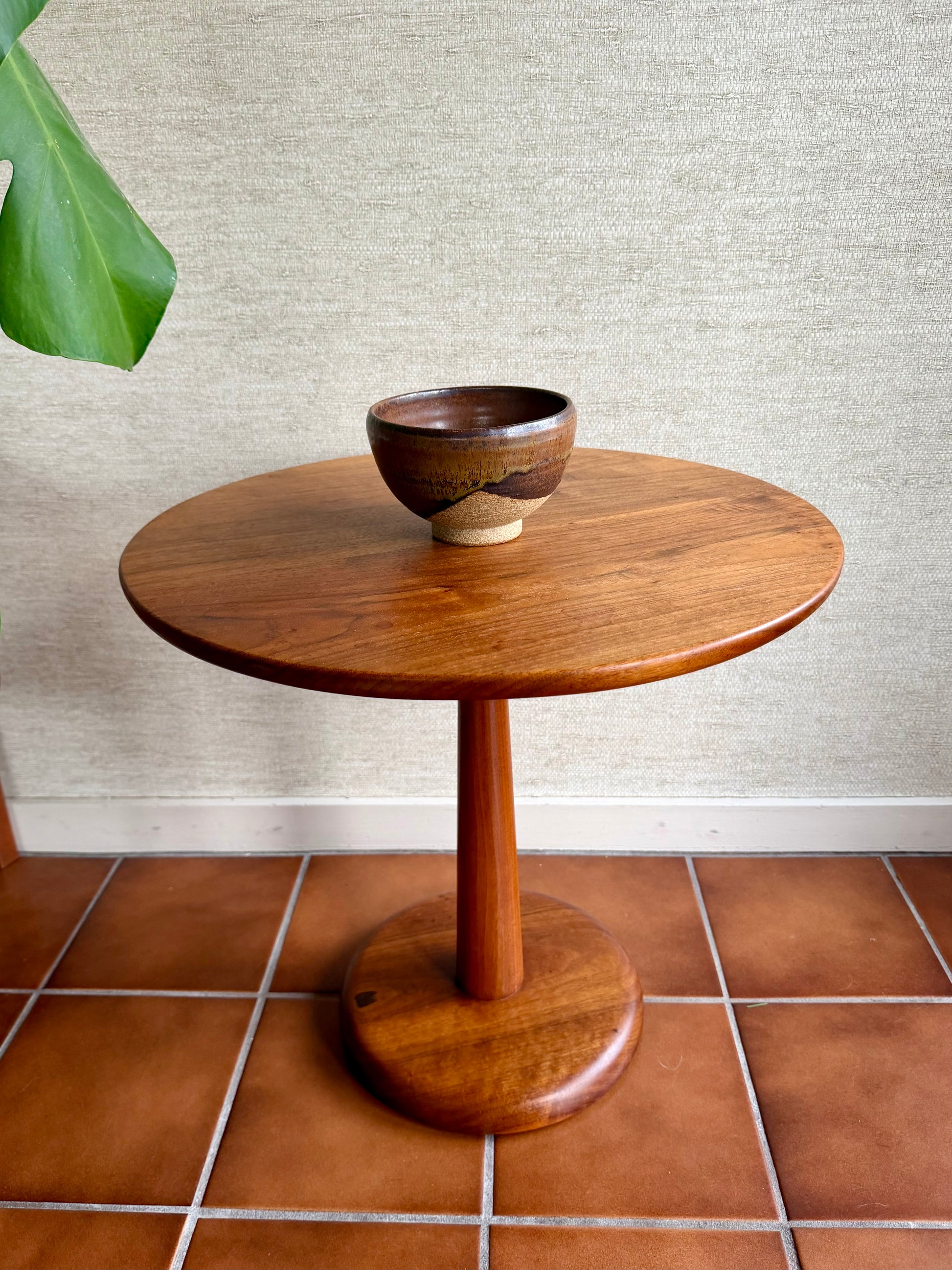 Wooden side table with a bowl on a tiled floor against a textured wall.