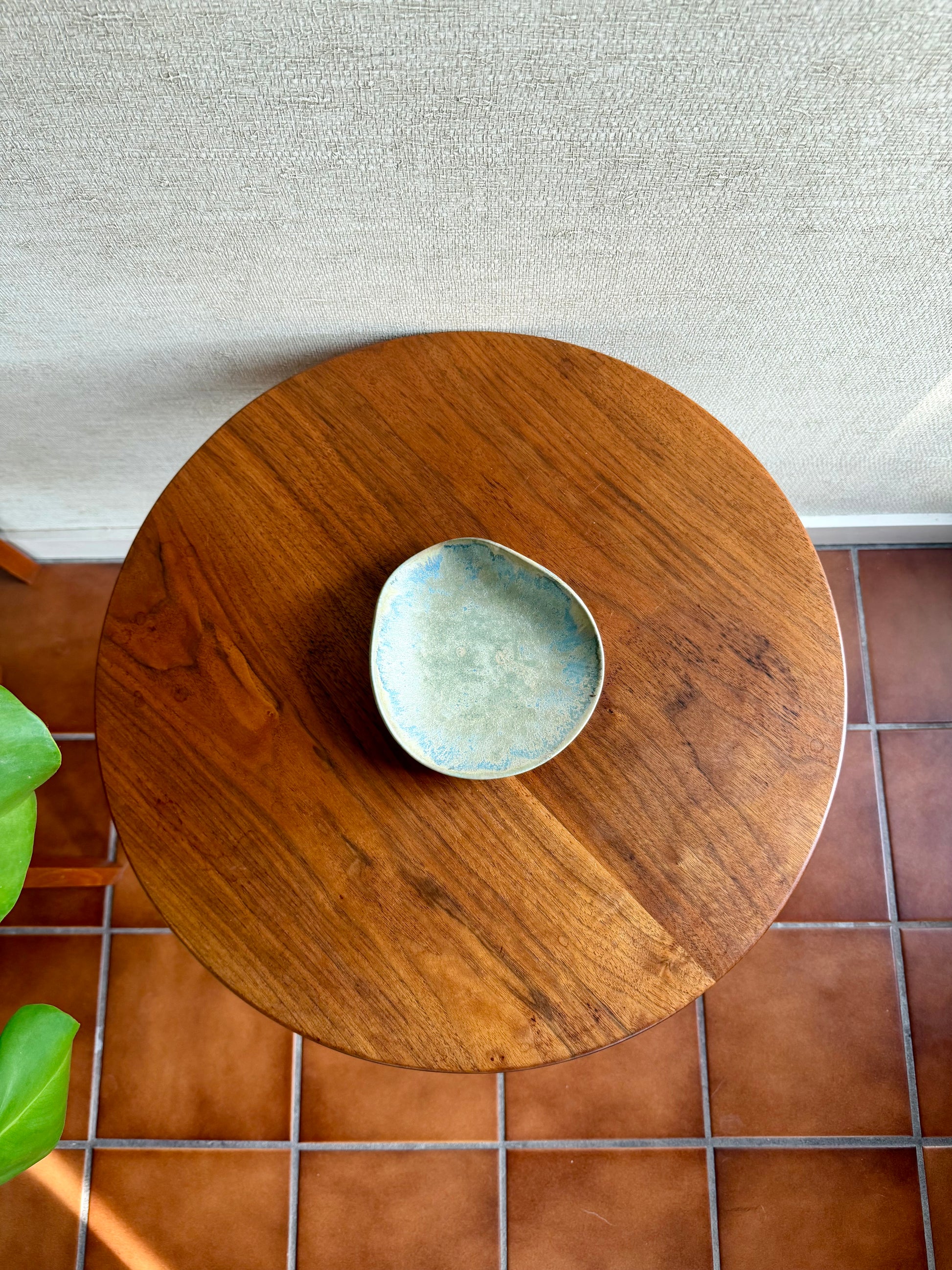 Wooden round table with a small decorative bowl on a tiled floor