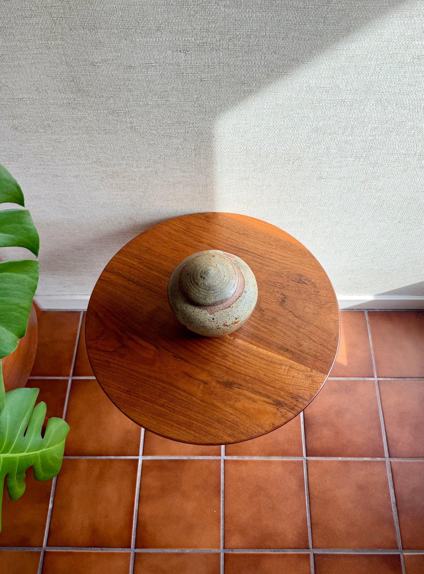 Small wooden table with a stone on top next to a plant on a tiled floor.