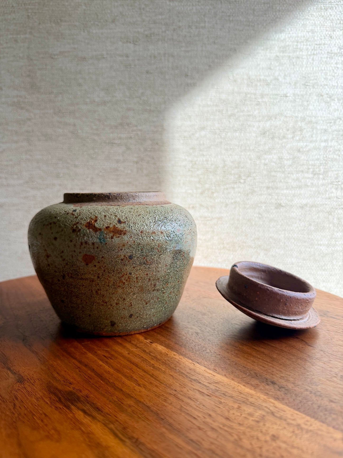 Two ceramic containers on a wooden surface with a textured wall background