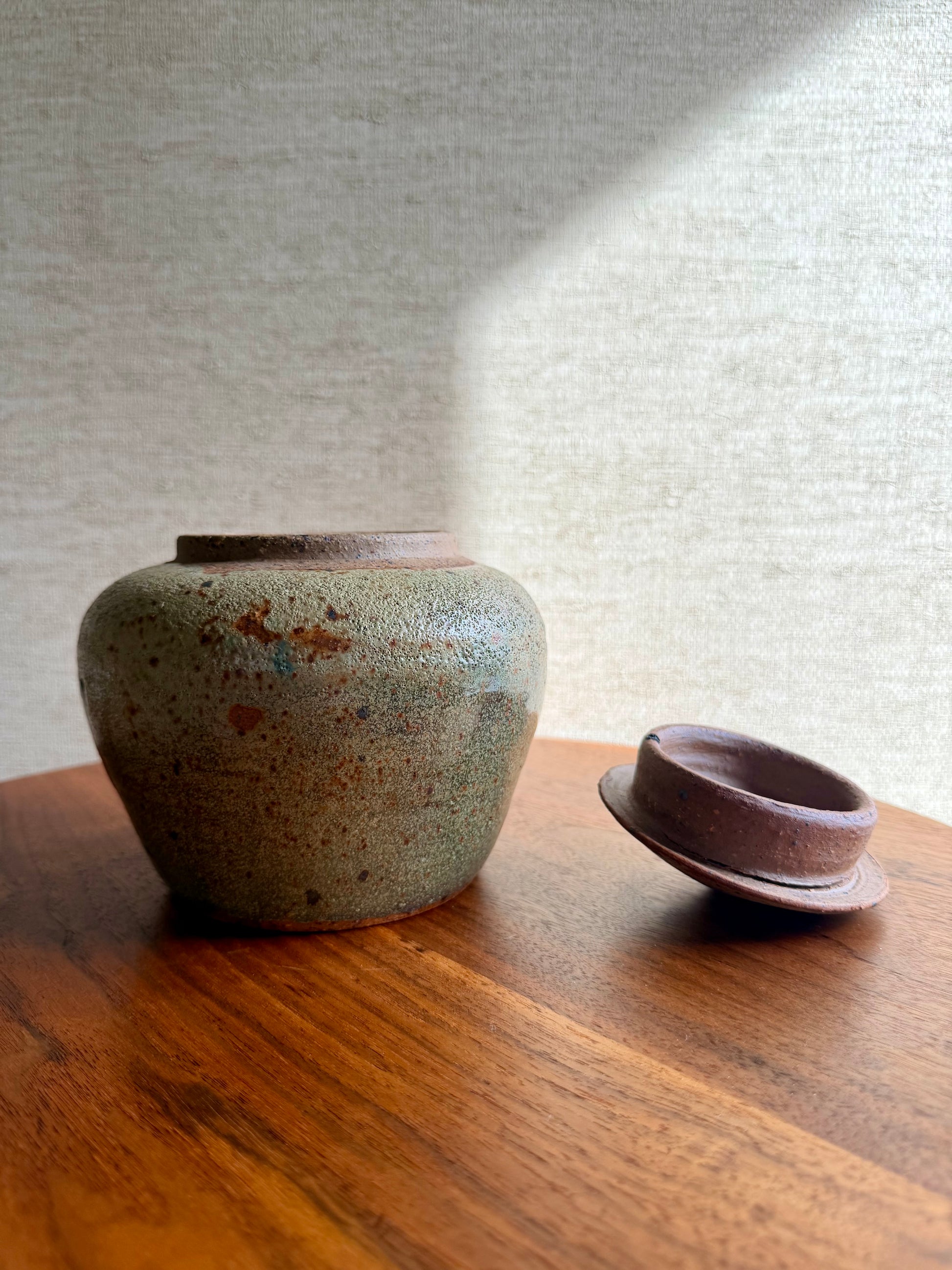 Two ceramic containers on a wooden surface with a textured wall background