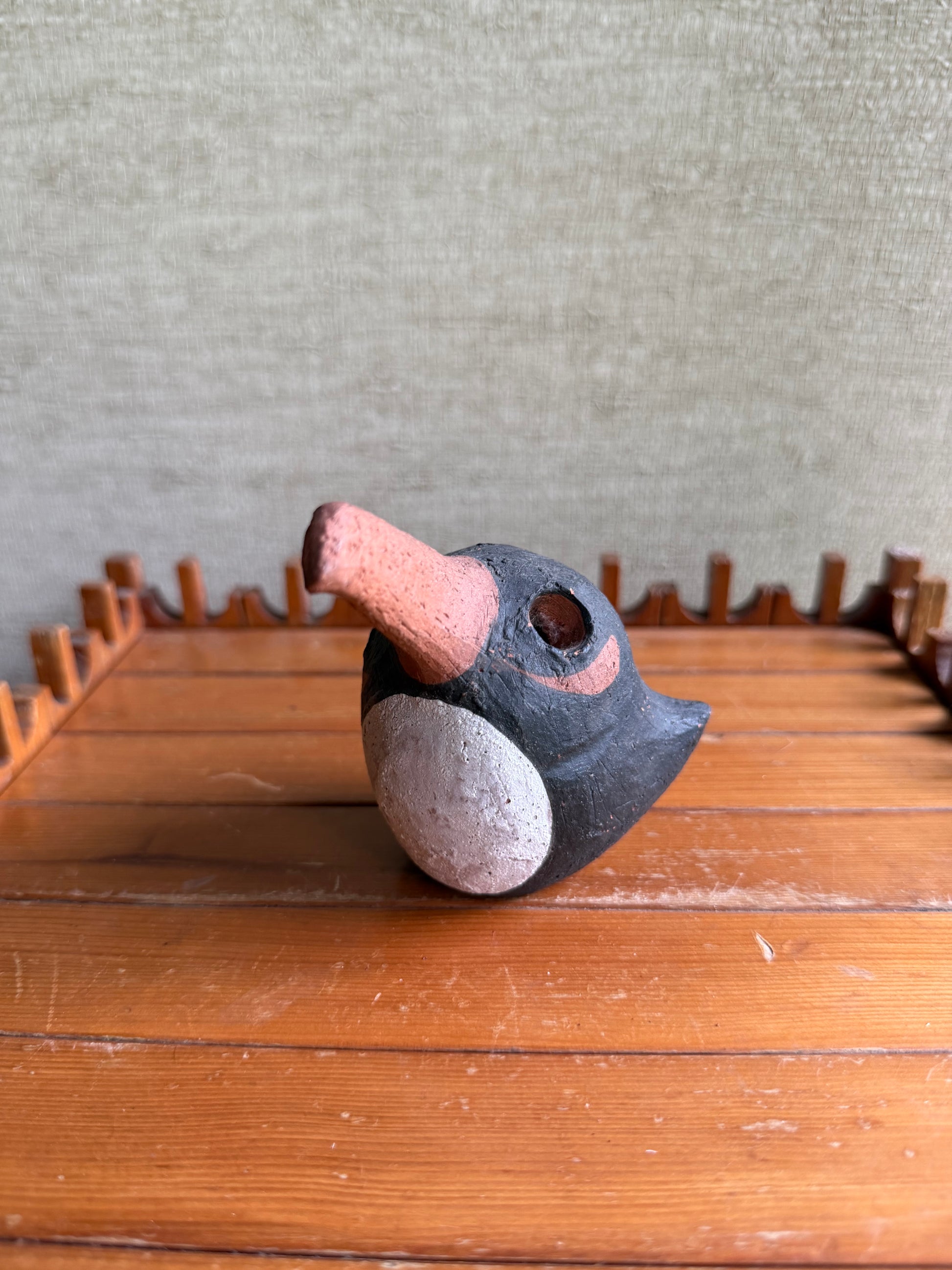 Ceramic bird figurine on a wooden surface with a textured wall background