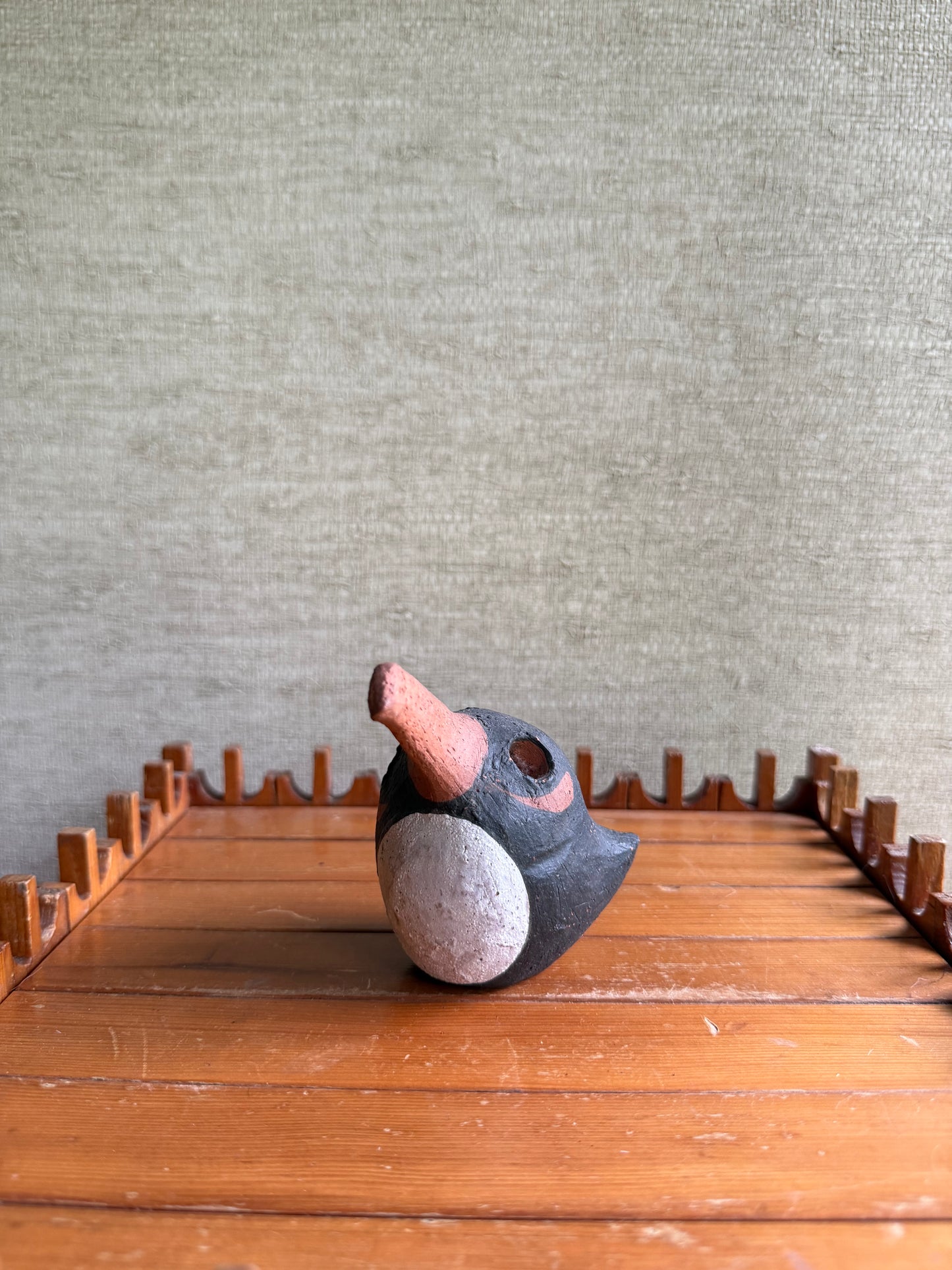 Decorative bird sculpture on a wooden surface with a textured wall background