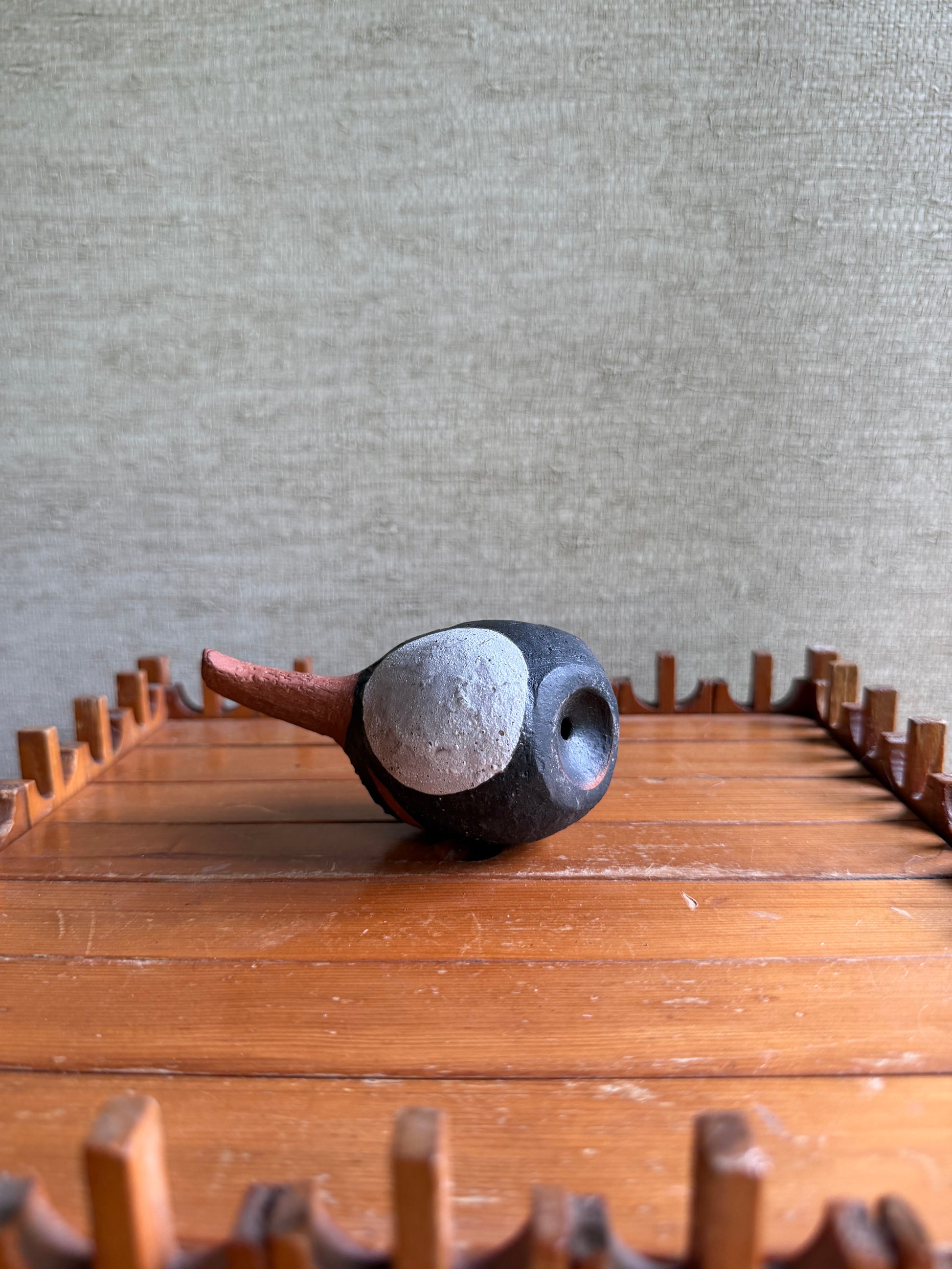 Ceramic bird with a textured surface on a wooden surface with a neutral background
