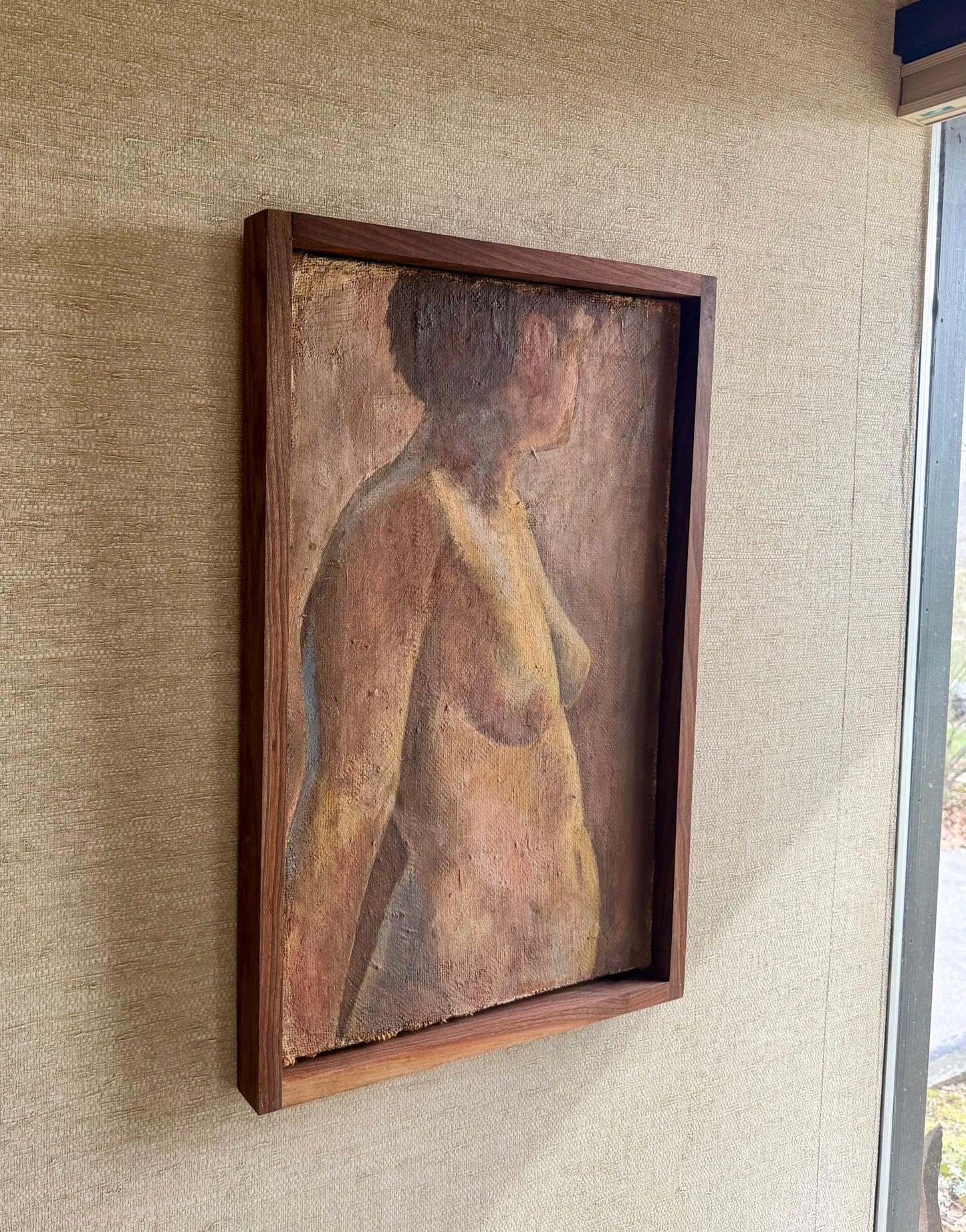 Framed painting of a nude figure on a textured wall.