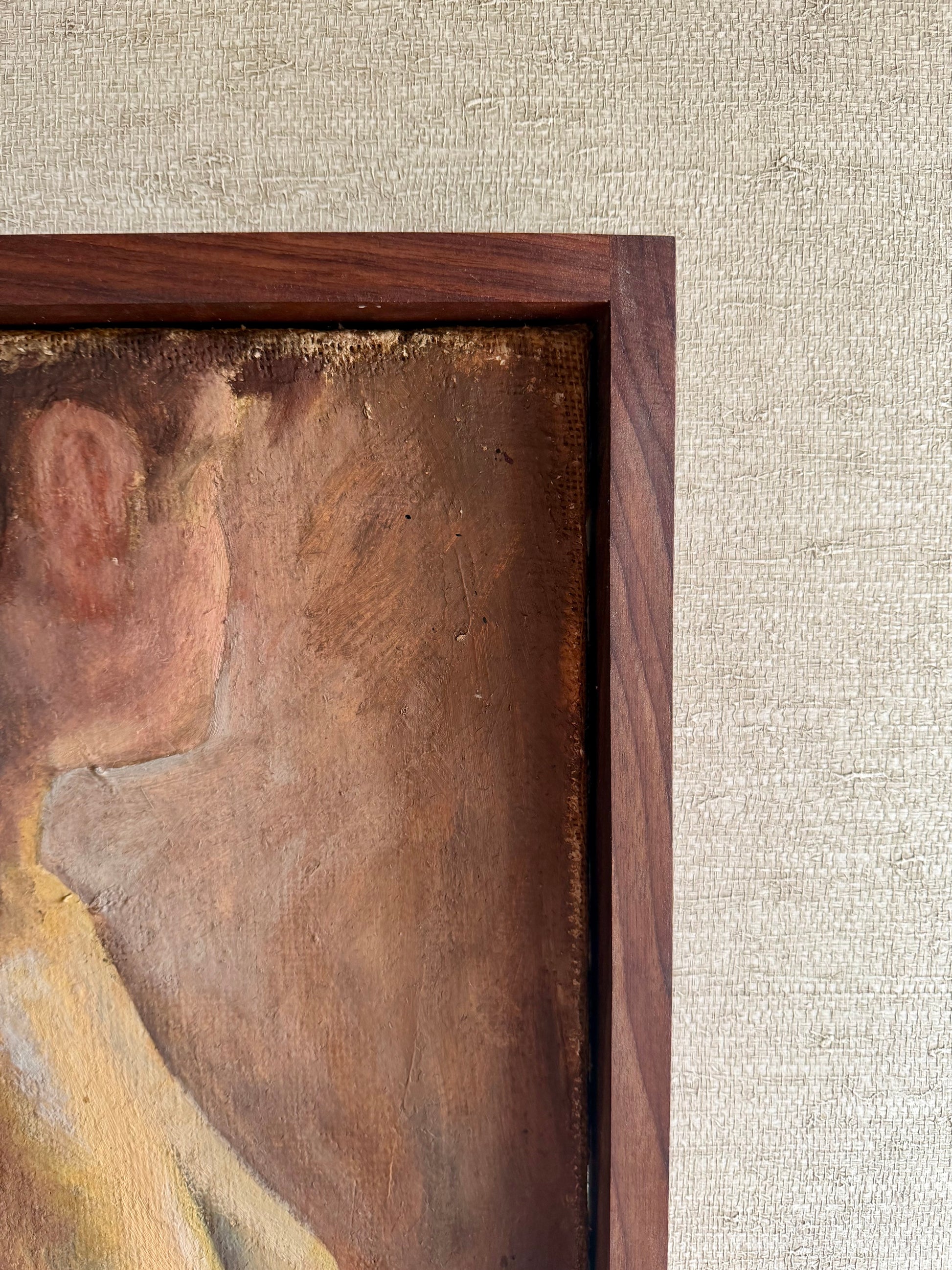 Close-up of a painting with a wooden frame on a textured beige wall.