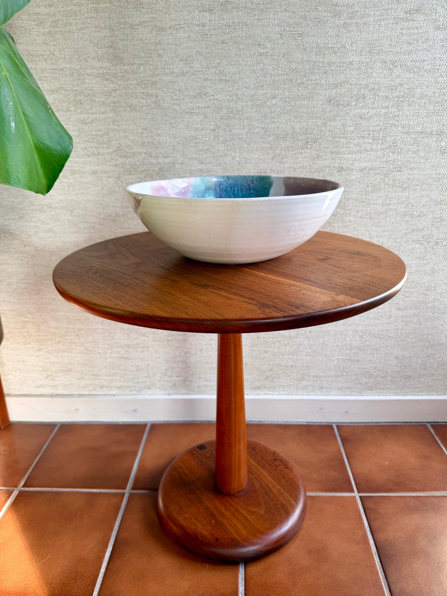 Wooden side table with a ceramic bowl on a tiled floor against a textured wall.