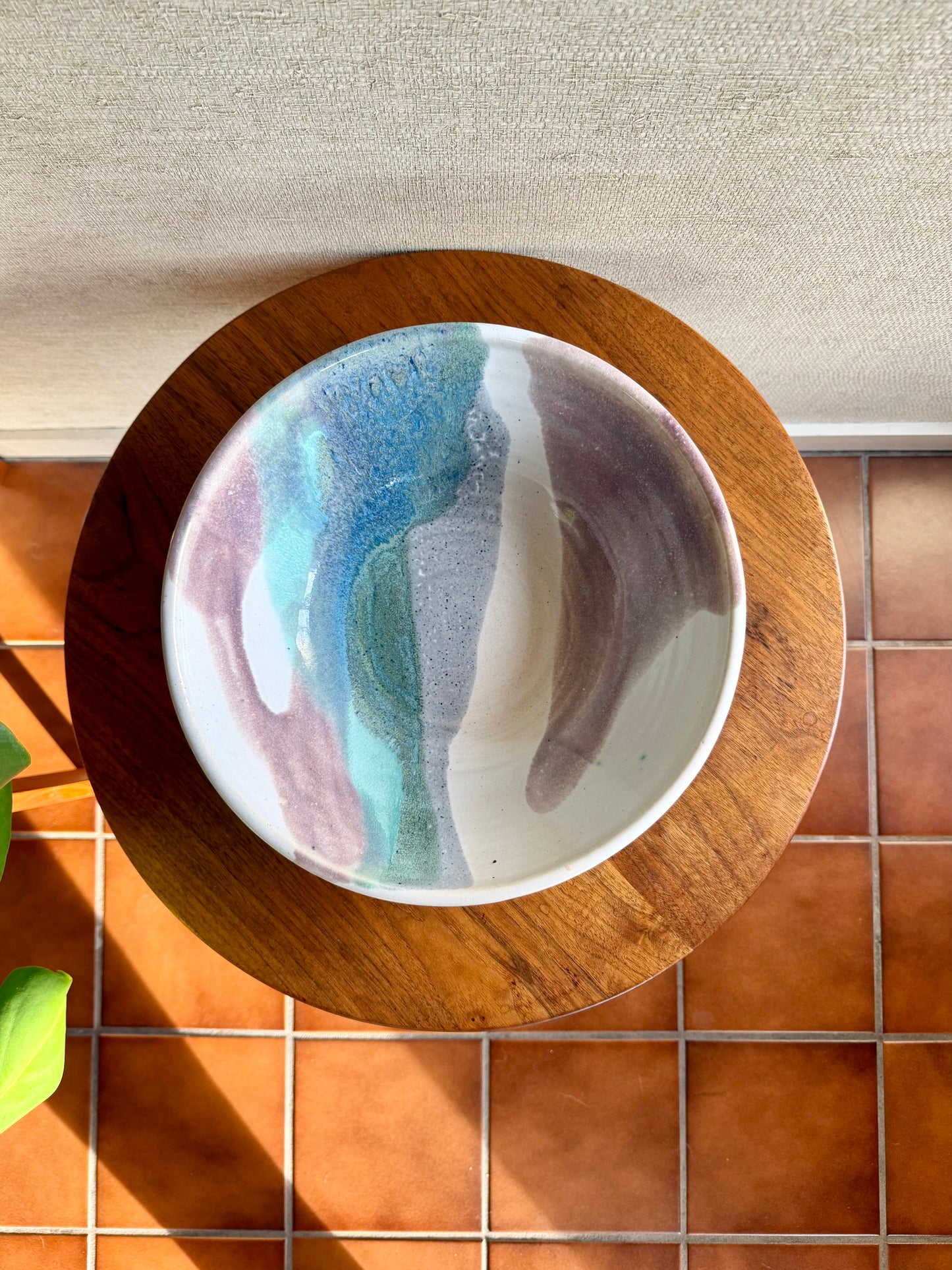 Decorative plate with abstract design on a wooden stand, placed on a tiled surface.
