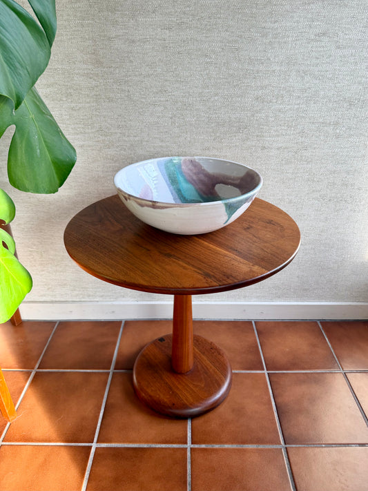 Small wooden table with a ceramic bowl on a tiled floor next to a plant.