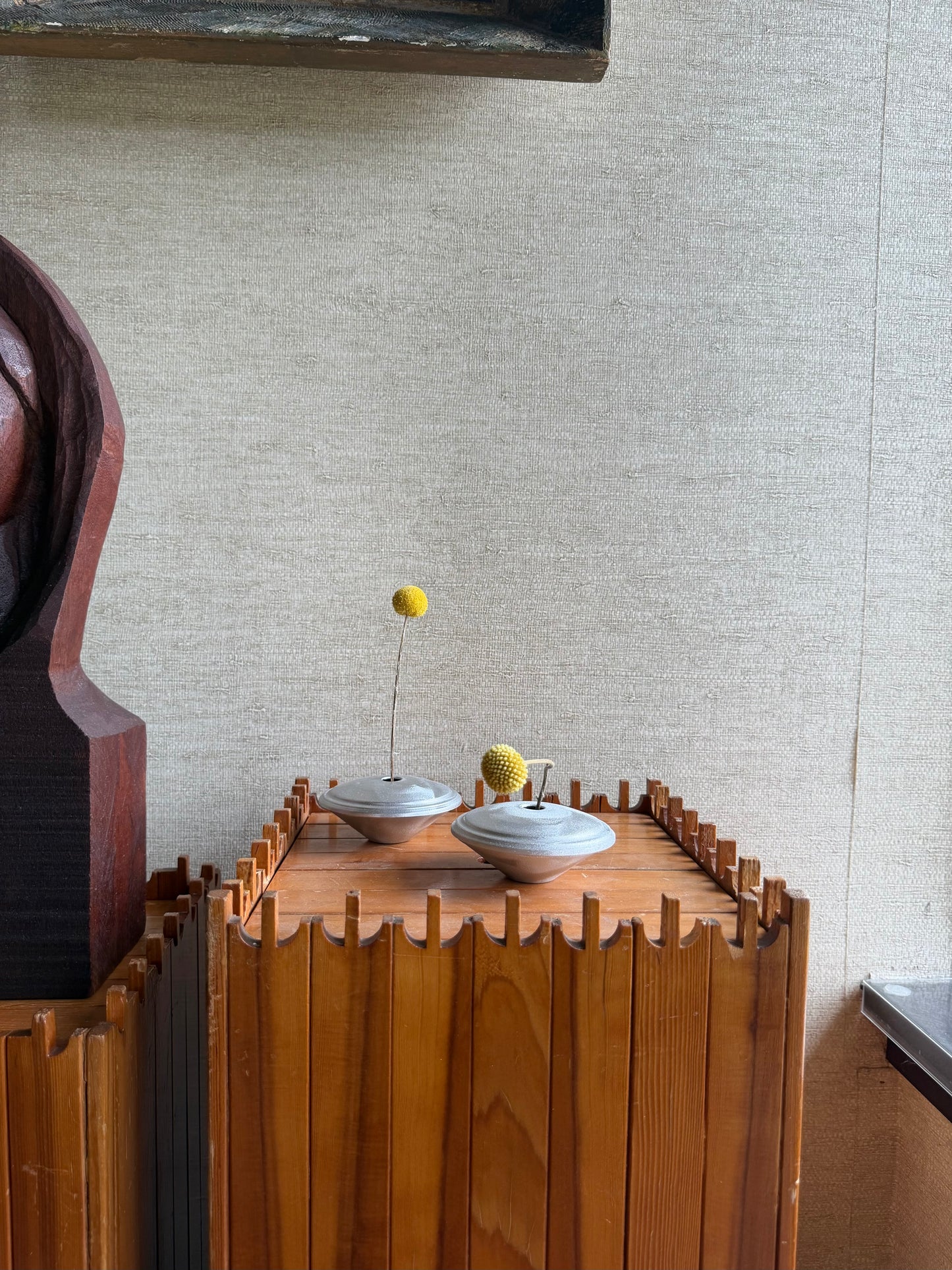 Wooden cabinet with two round bowls and a small plant against a textured wall.