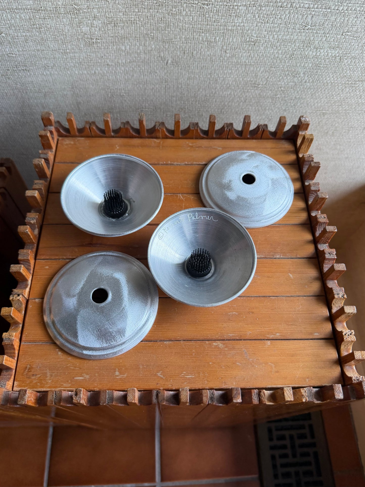Three metal bowls on a wooden stand against a textured wall.
