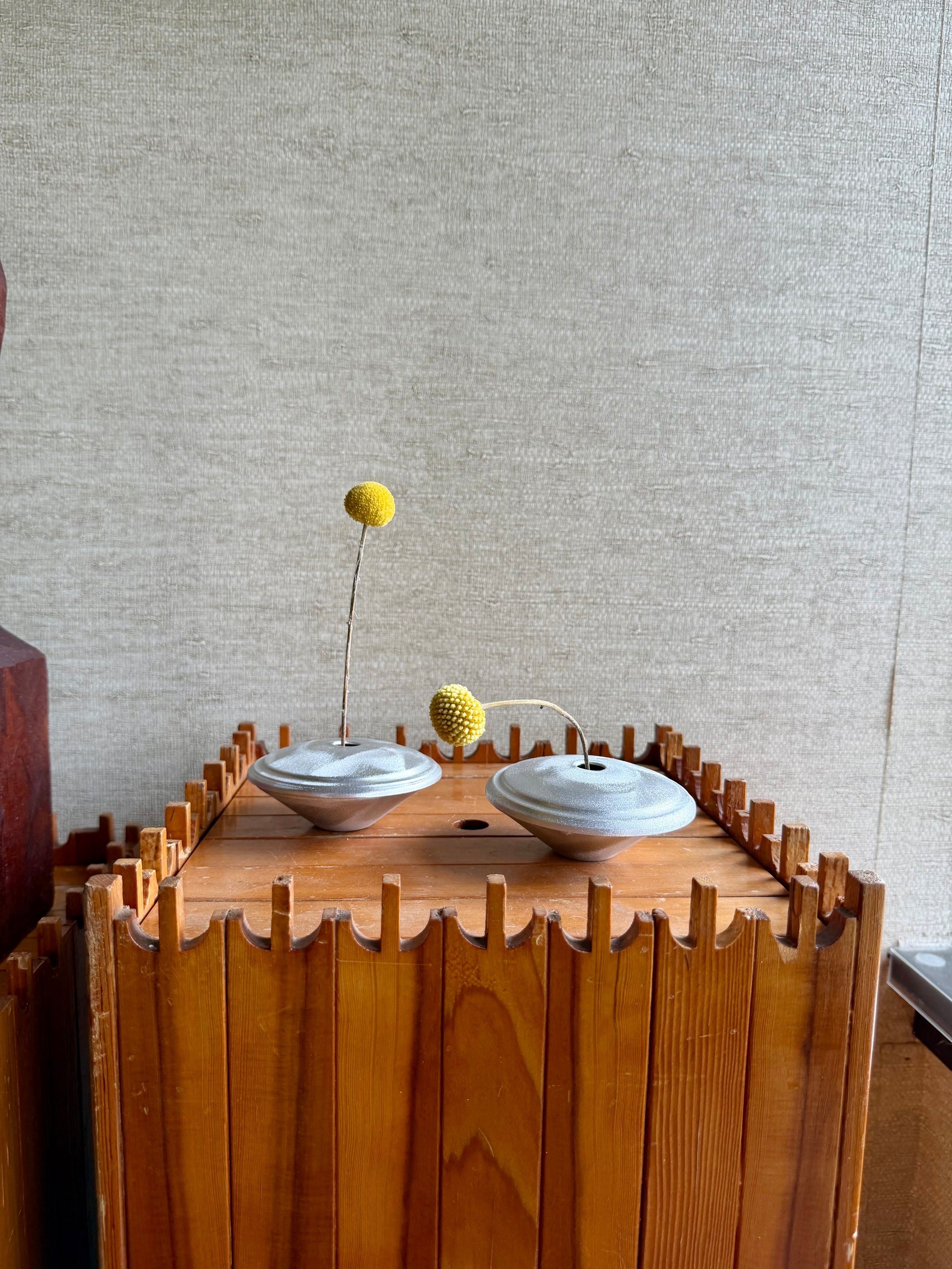 Two white bowls with a yellow ball on a wooden stand against a textured wall.