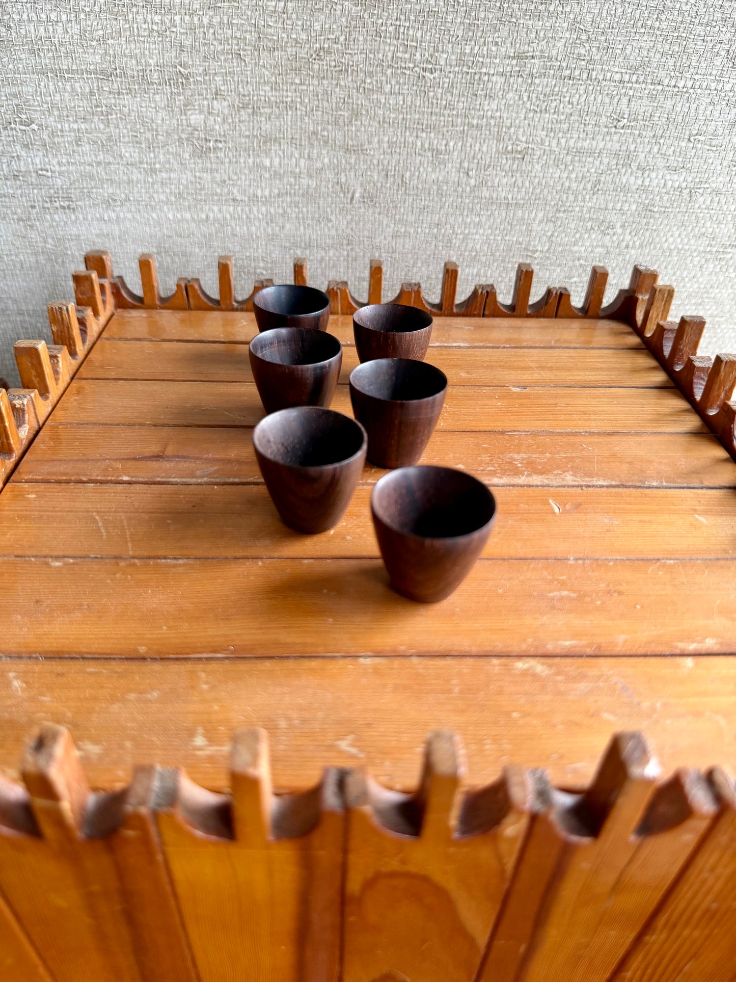 Wooden tray with six dark wooden cups on a textured wall background