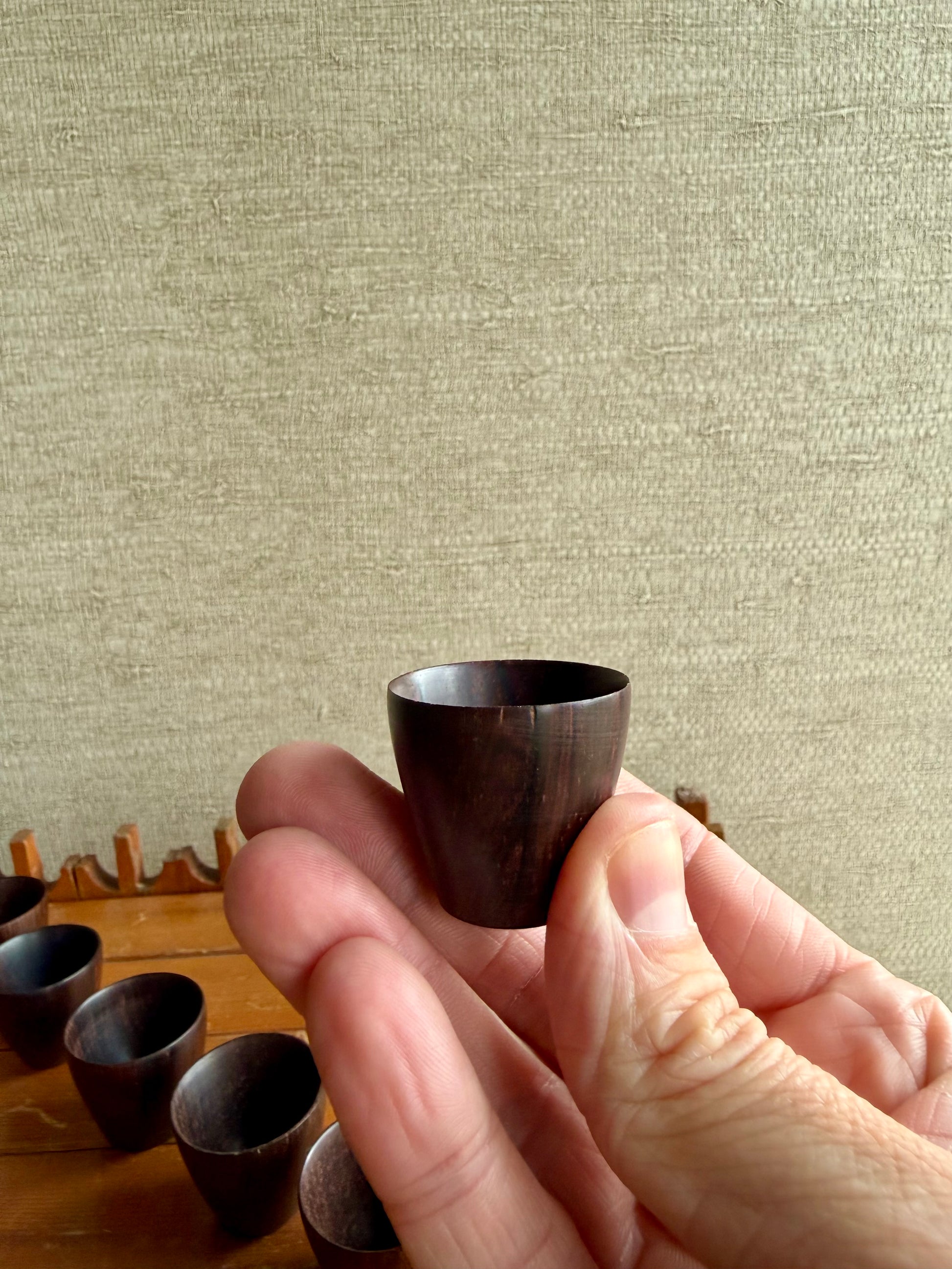 Hand holding a small wooden cup against a textured beige background