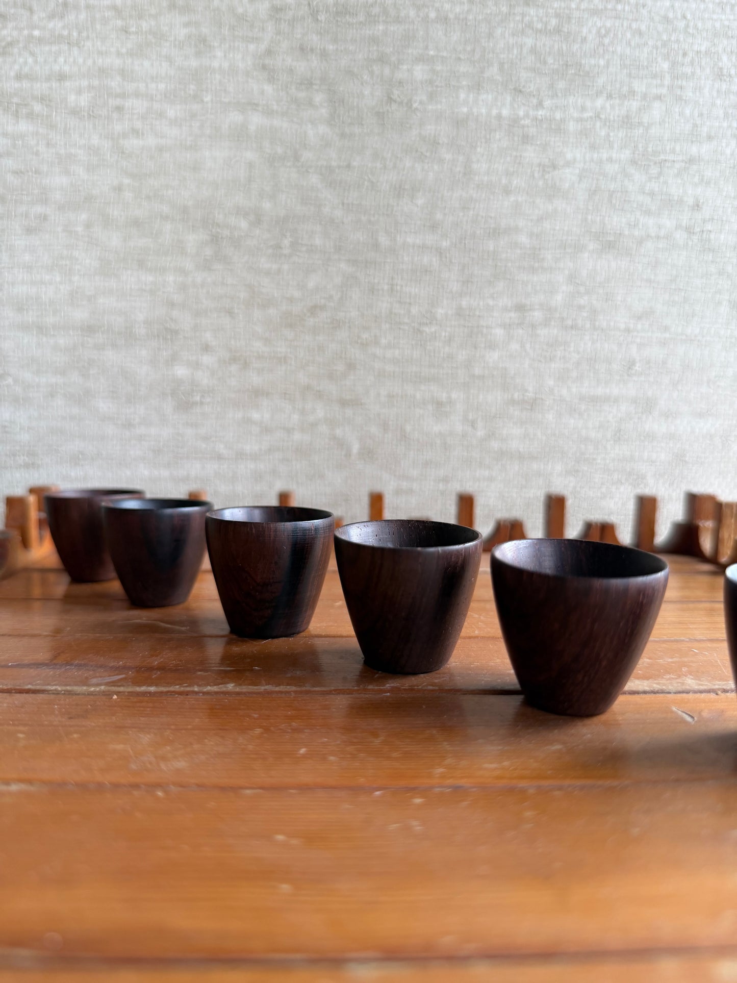 Set of dark wooden cups on a wooden surface with a textured light gray wall in the background.