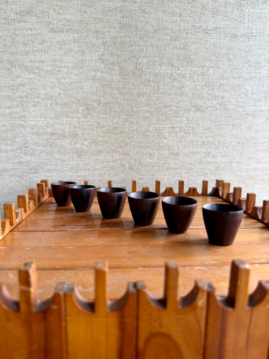 Row of wood cups on a wooden stand against a textured light gray wall.