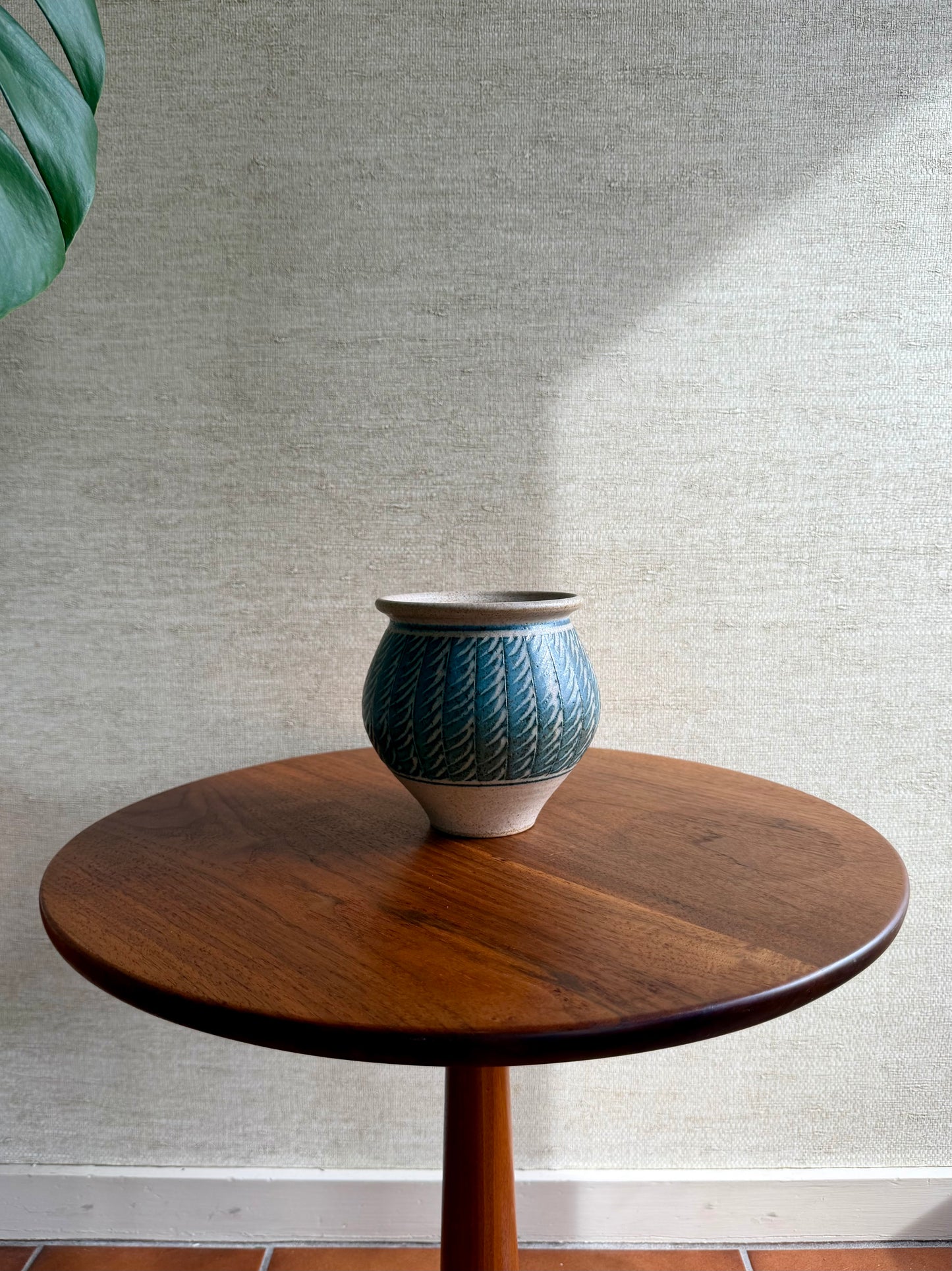 Blue ceramic vase on a wooden table against a textured wall.
