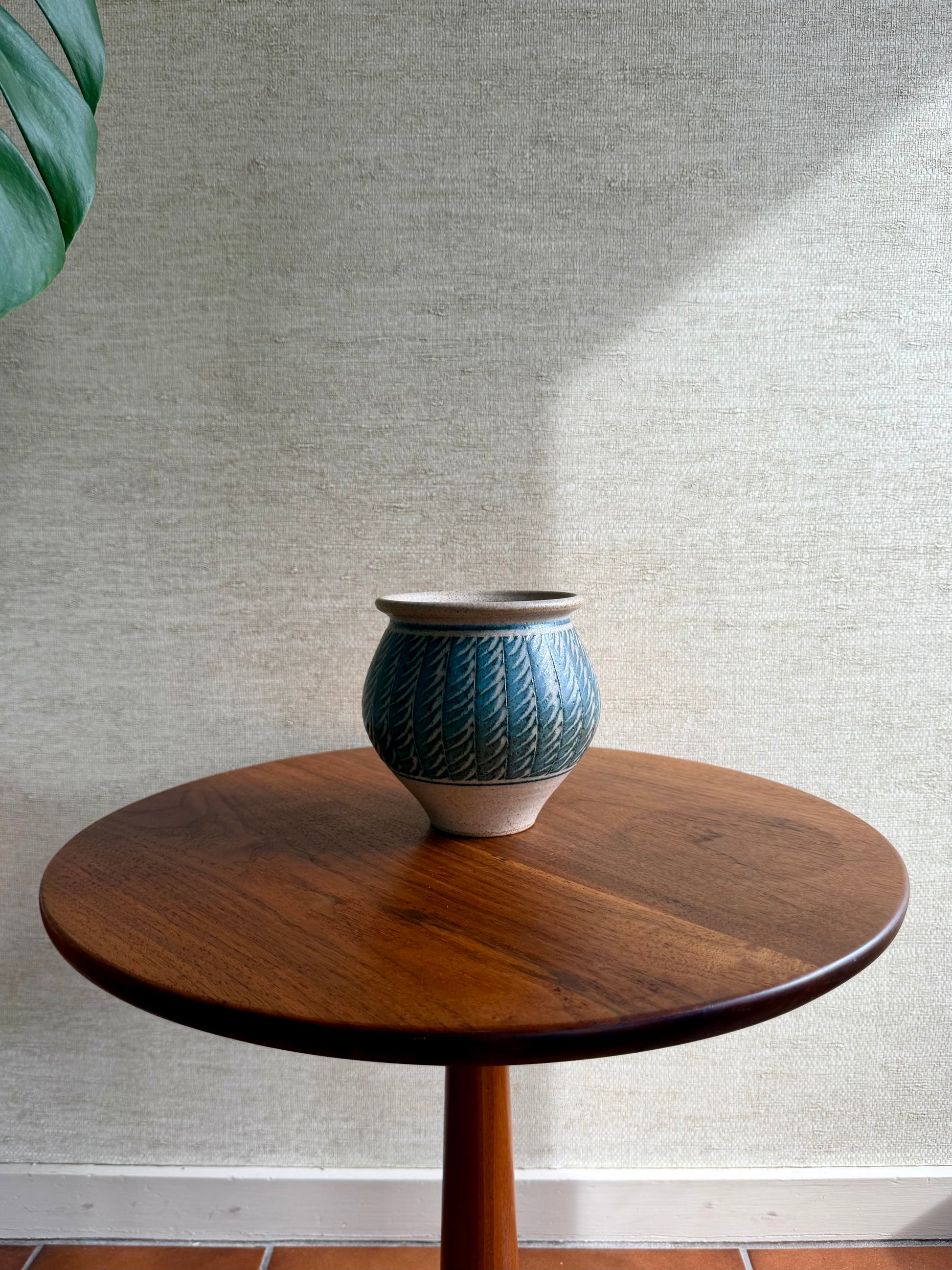 Blue ceramic vase on a wooden table against a textured wall.