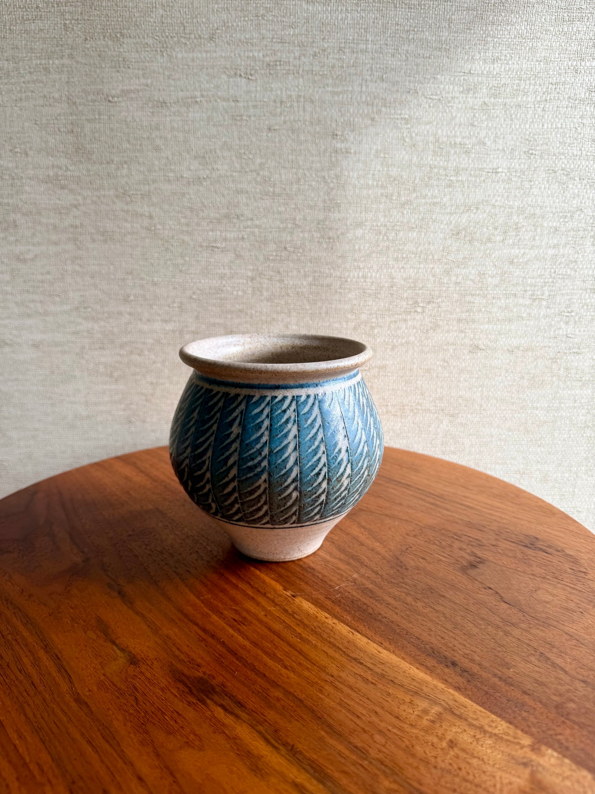 Blue ceramic pot with textured design on a wooden table against a gray wall