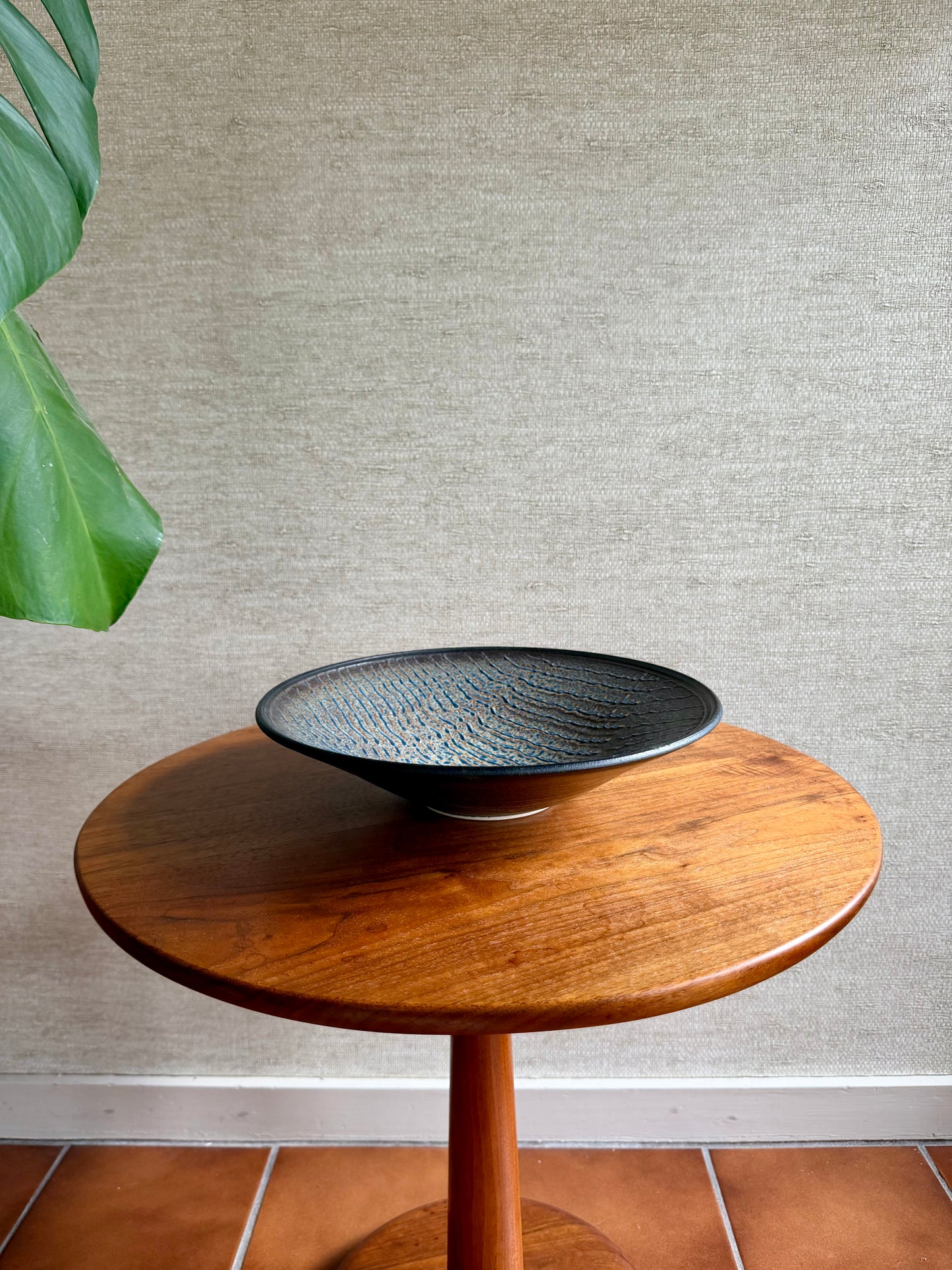 Wooden side table with a black textured bowl on a neutral wall background