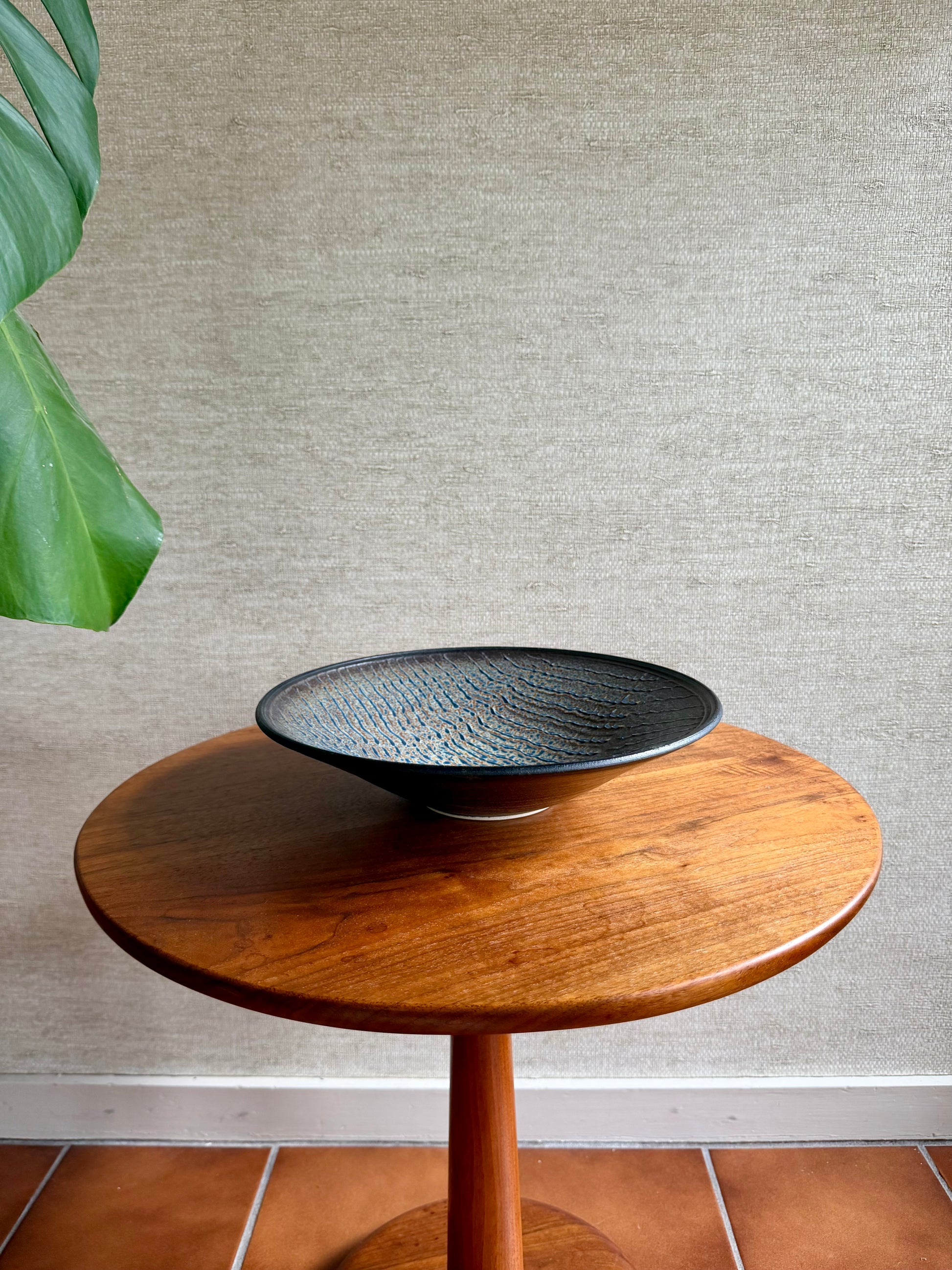 Wooden side table with a black textured bowl on a neutral wall background