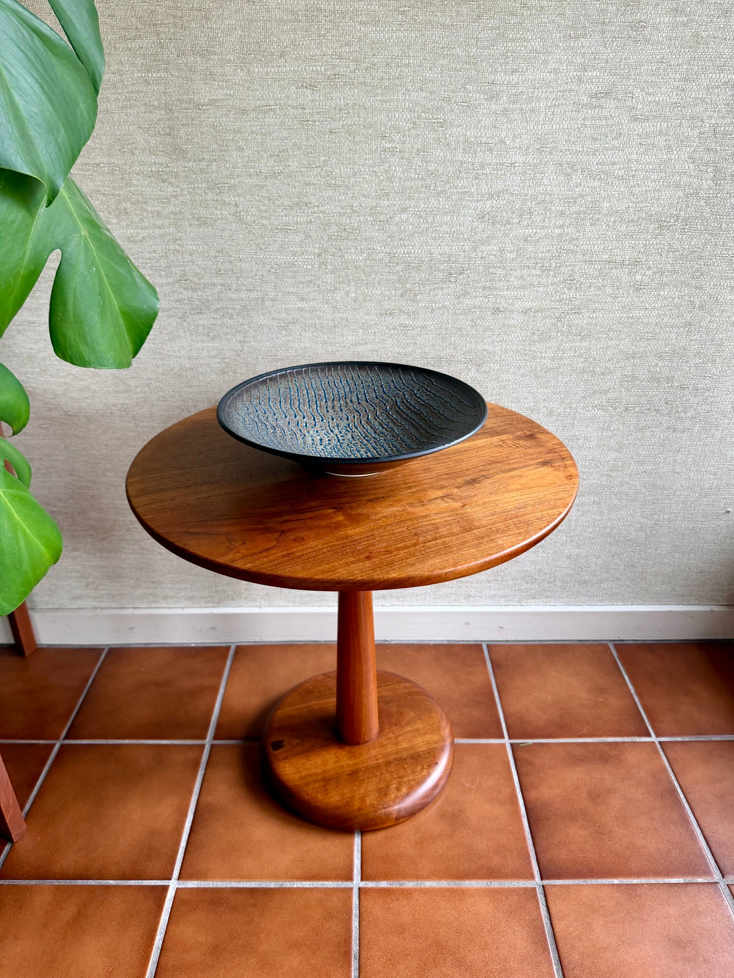 Wooden side table with a black bowl on a tiled floor against a textured wall.