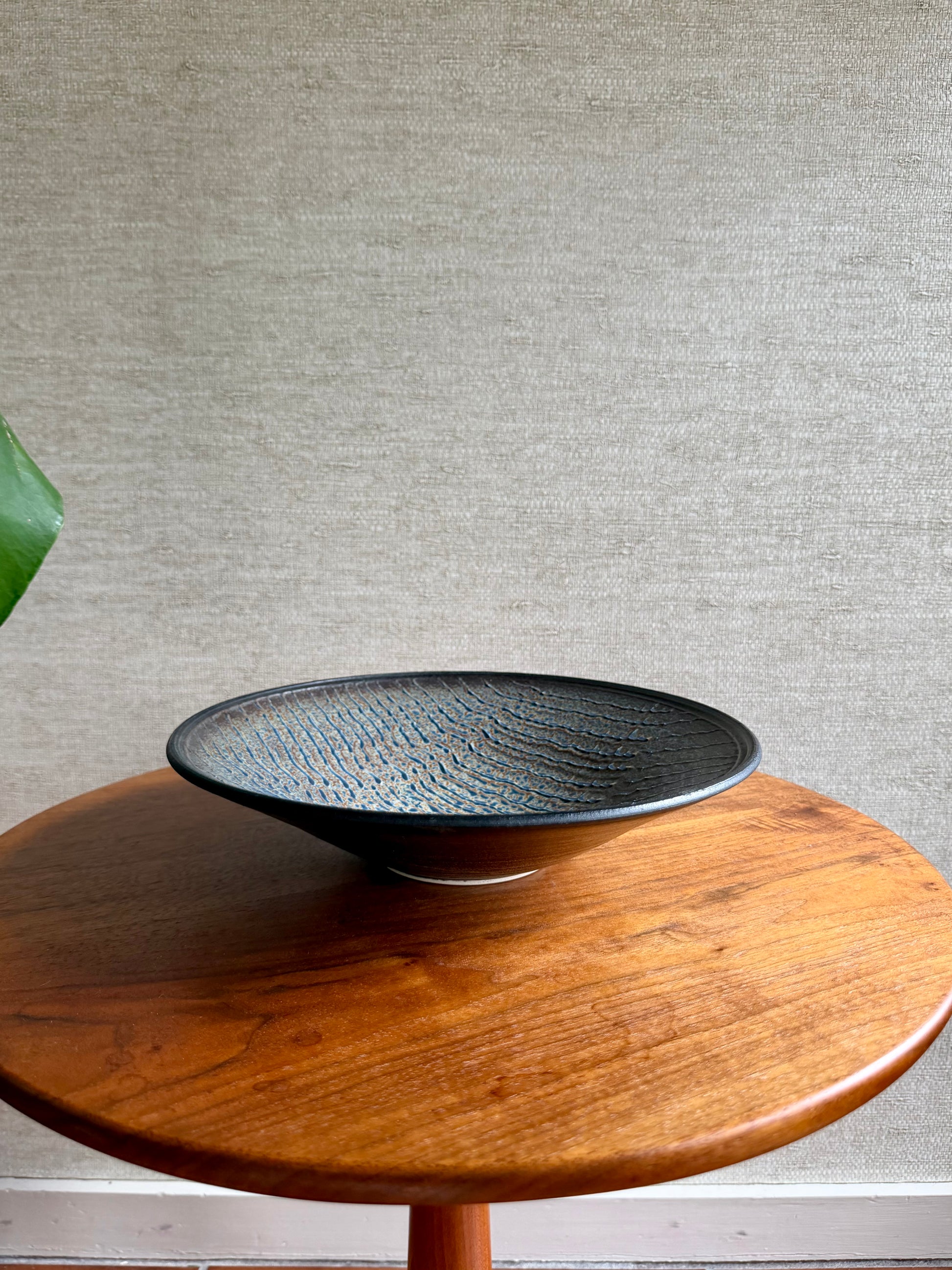 Black textured bowl on a wooden table with a gray textured wall background